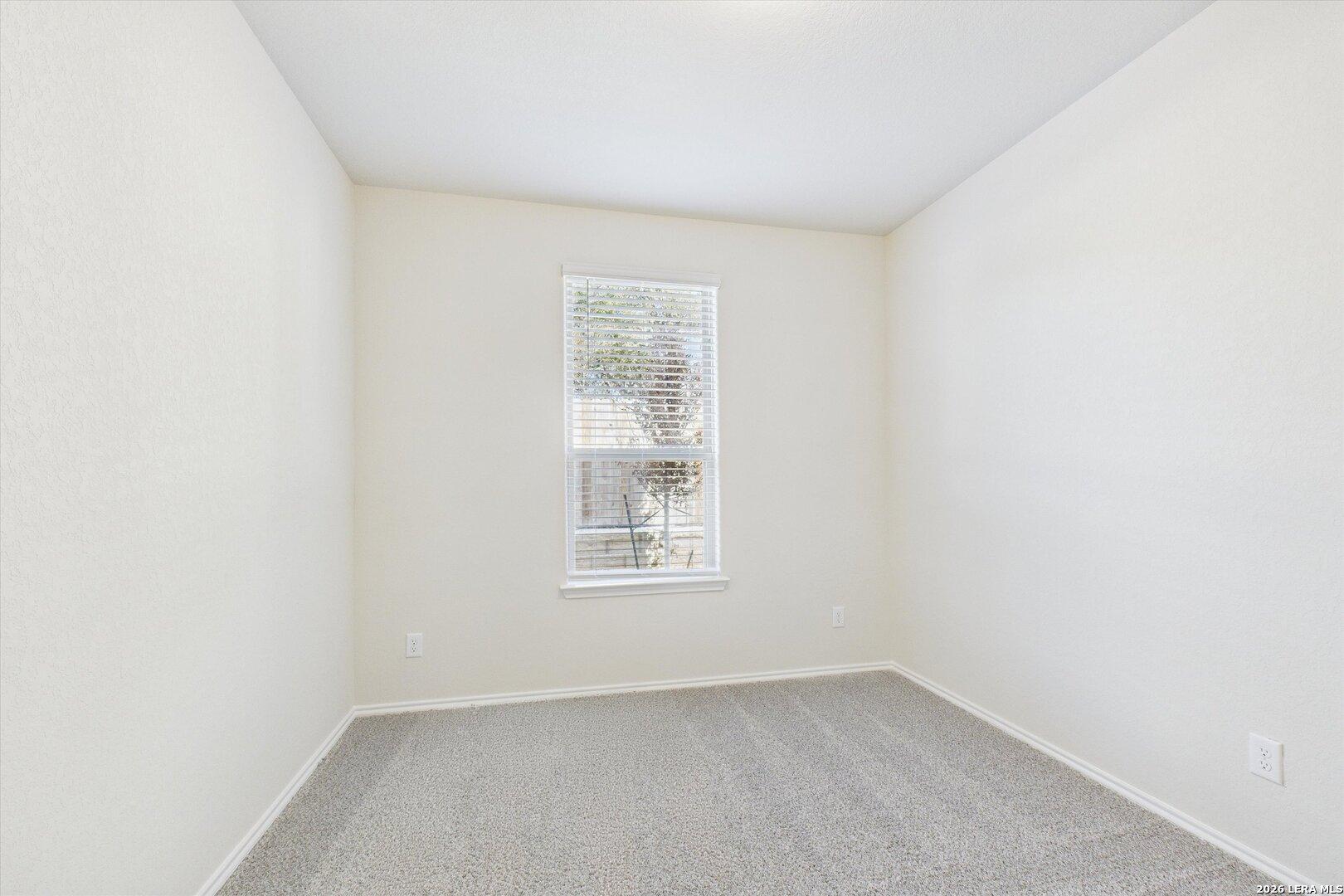 Bright secondary bedroom with neutral beige walls, plush carpet, and large window in Davidson Homes The Gillian B, San Antonio, Texas