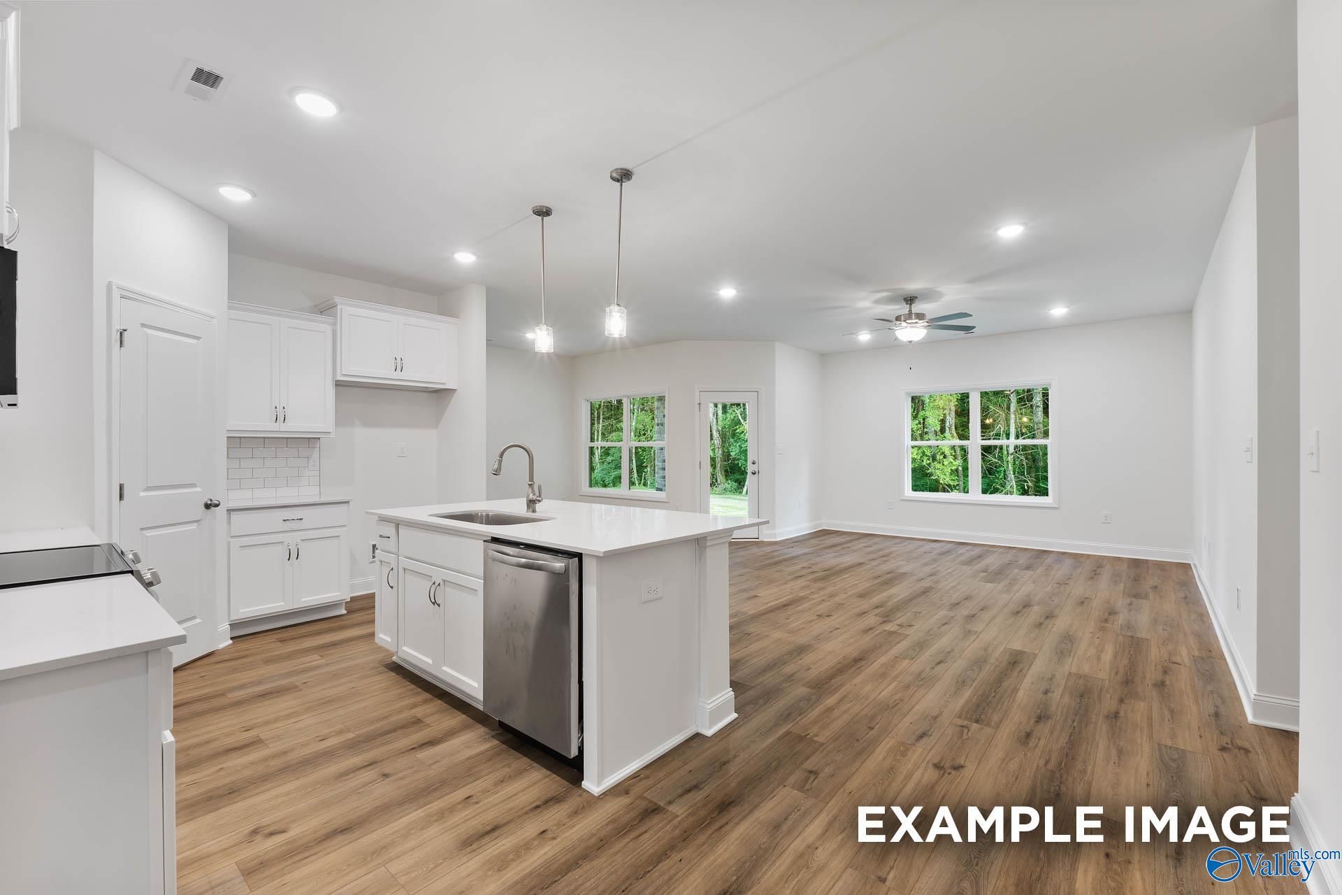Open-concept kitchen with white shaker cabinets, quartz island, stainless sink, and backyard views via French doors in The Daphne V, Chapel Hill, Athens, Alabama