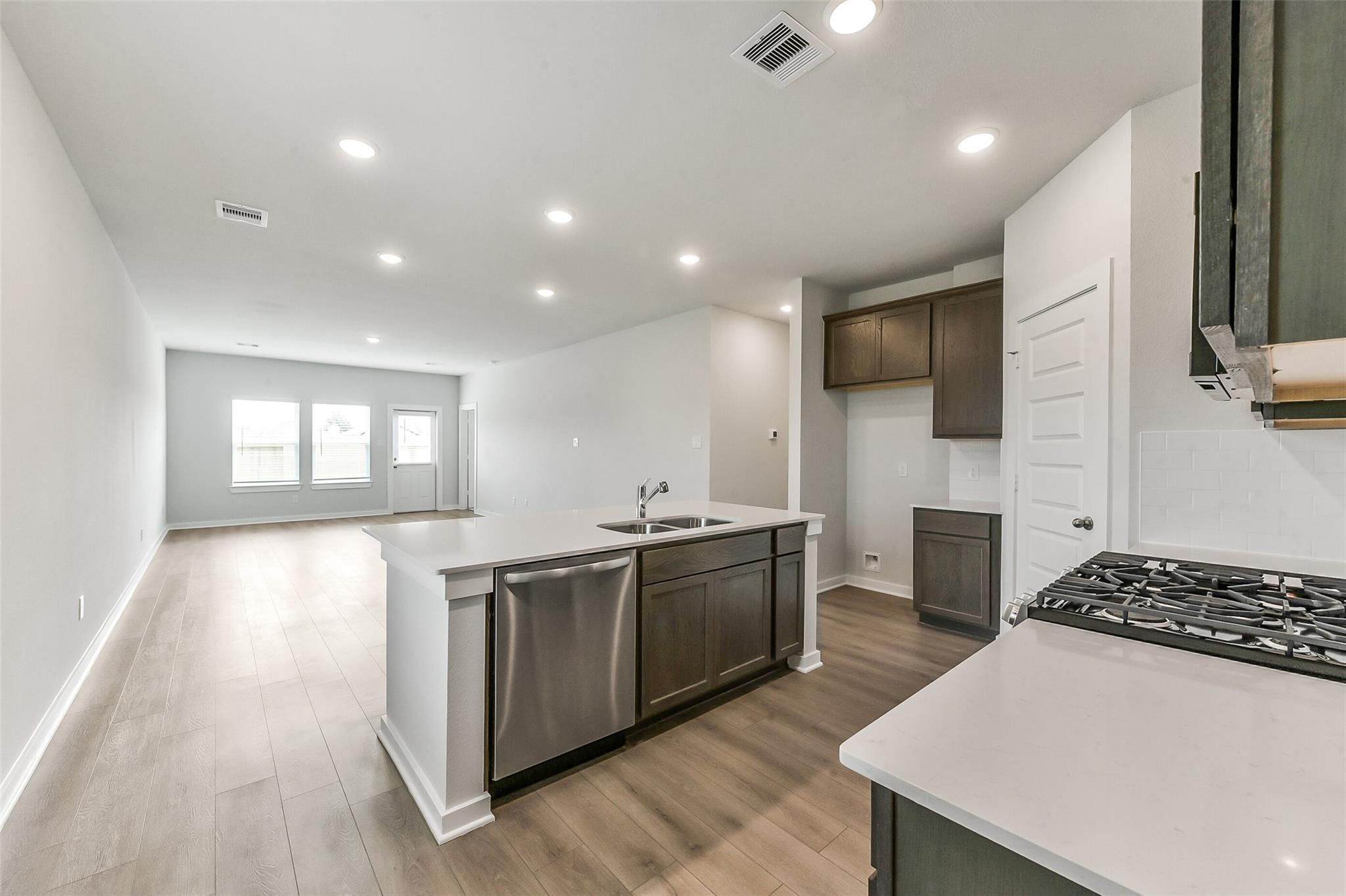 Modern open-concept kitchen with quartz island, stainless dishwasher, gas range, shaker cabinets in The Sabine F by Davidson Homes, Dayton TX