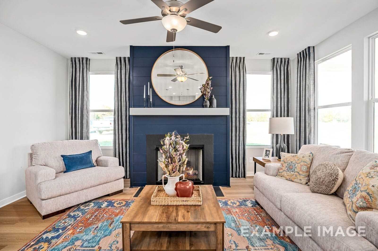 Cozy living room with navy blue fireplace, round mirror, beige sofas, and colorful rug in Davidson Homes Franklin B, Sage Farms, White House, Tennessee