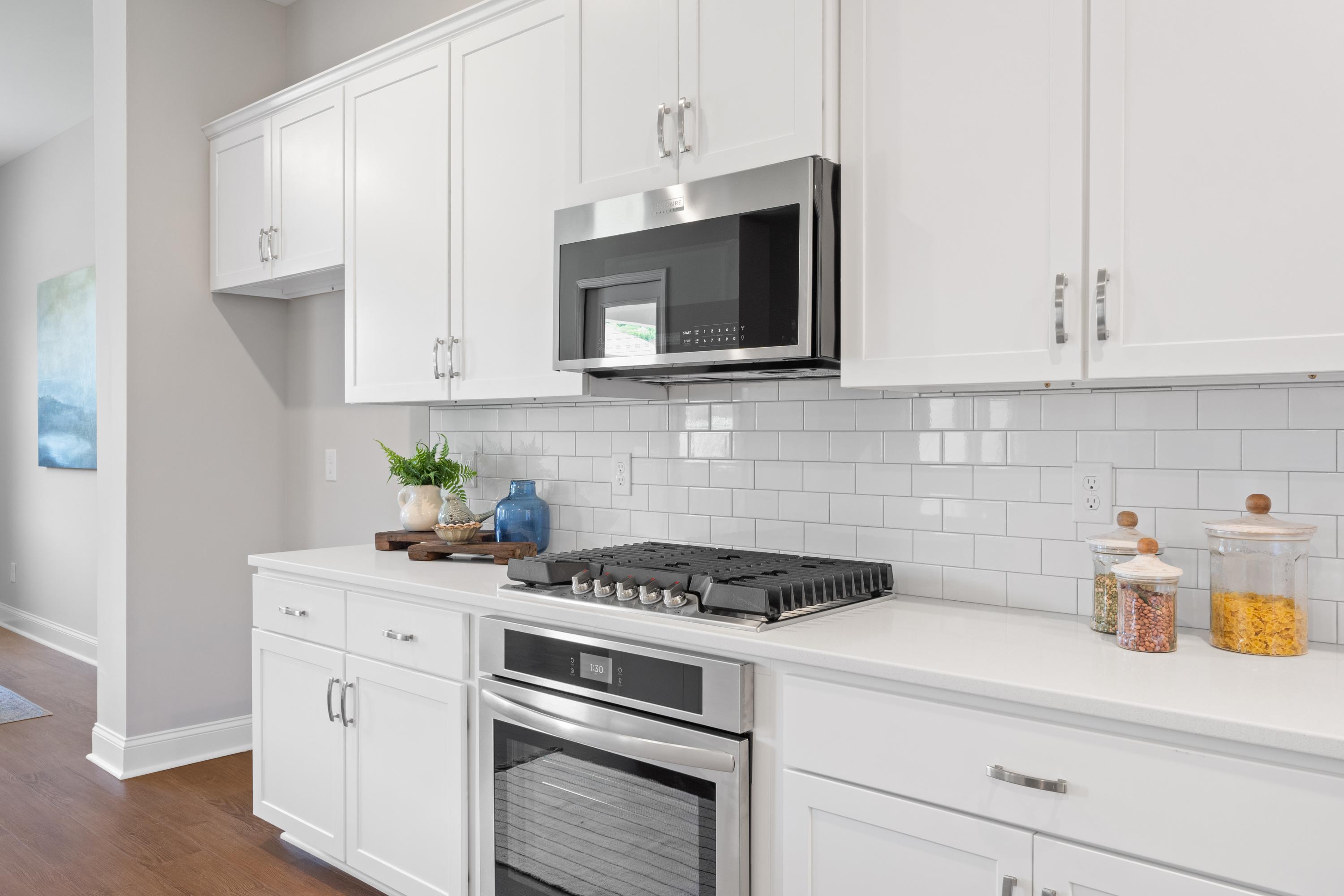 Spacious kitchen in The Haven home design by Evermore Homes featuring white shaker cabinets, stainless steel gas range, and subway tile backsplash
