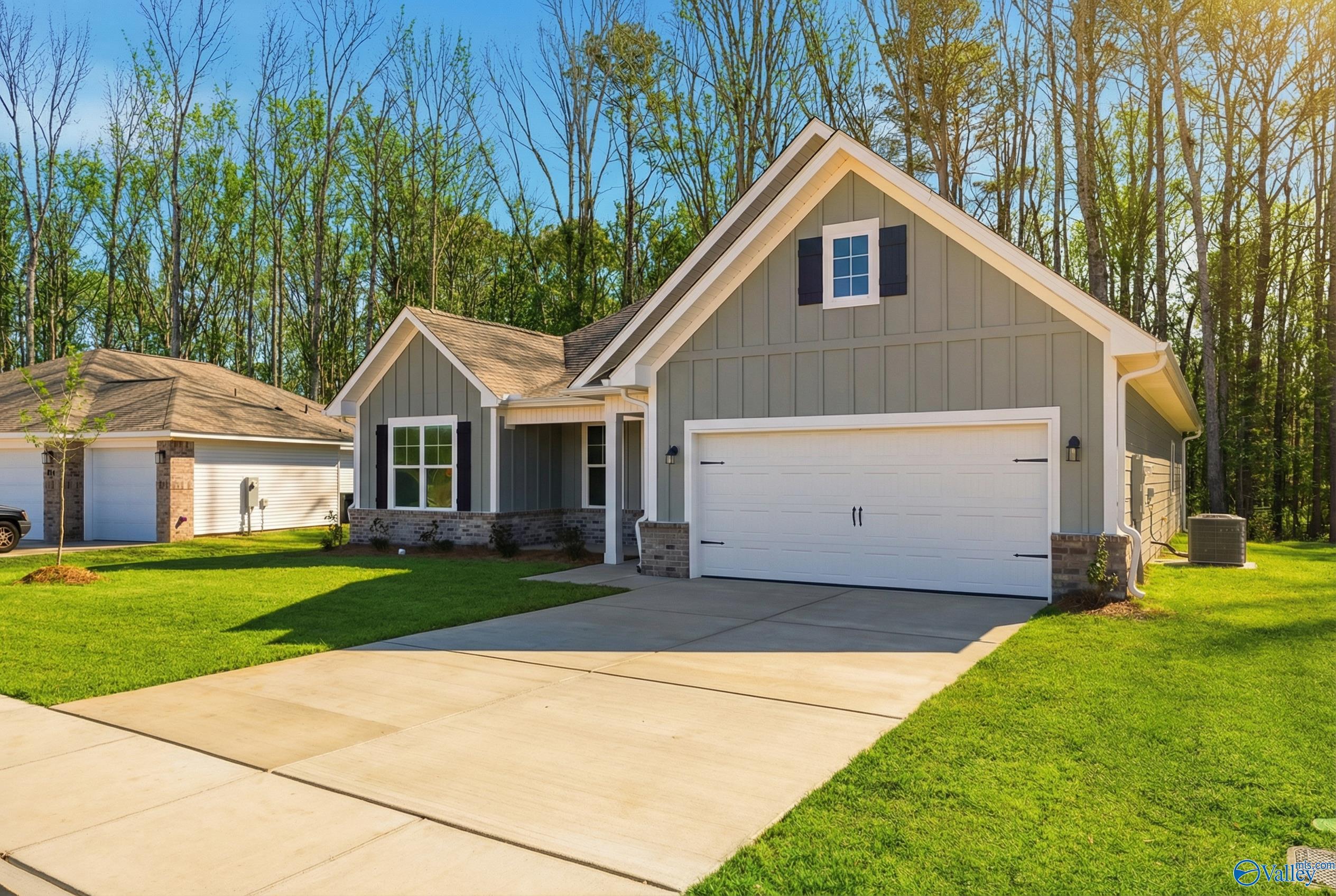 Modern gray 1-story Davidson Homes The Rockford D with 2-car garage, driveway, green lawn, and wooded backdrop in Forest Glen, Hazel Green, Alabama