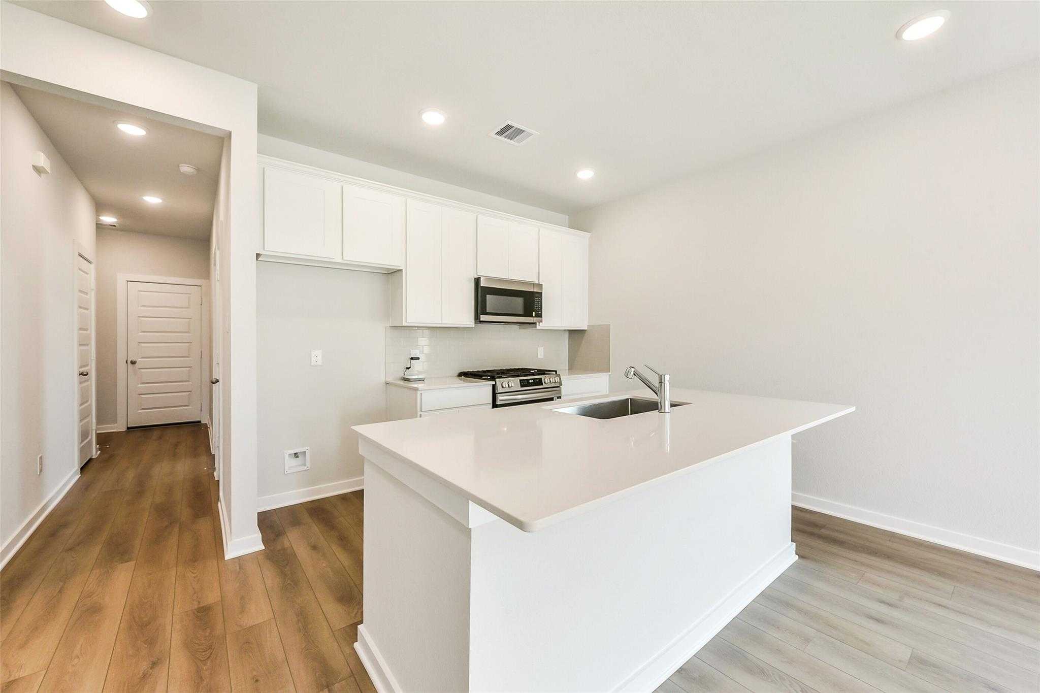 Modern white kitchen with quartz island, stainless steel appliances, and open layout in The Comal G home, Dayton, Texas