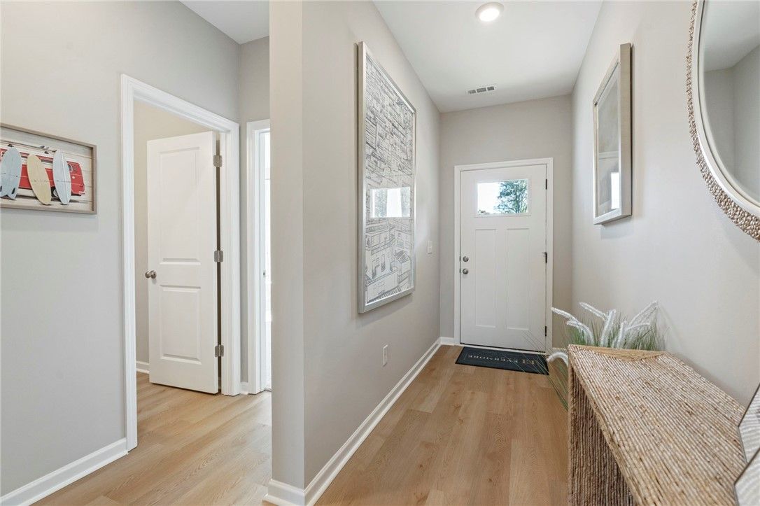 Bright entry foyer with wood flooring, white front door, framed art, round mirror, and woven bench in Davidson Homes The Phoenix B, Opelika