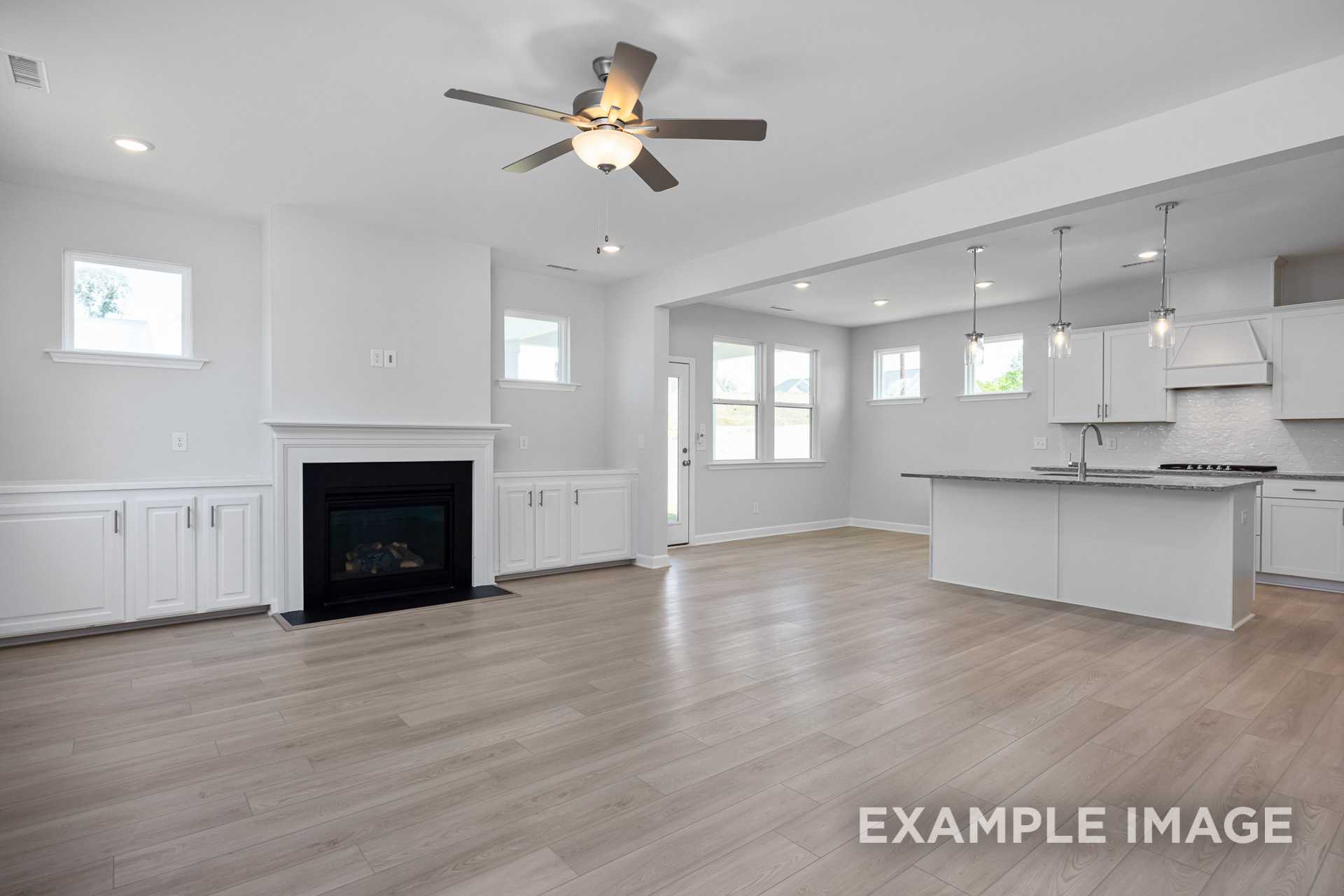 Spacious open-concept kitchen and living area in The Gavin C featuring white island, gas fireplace, and ceiling fan