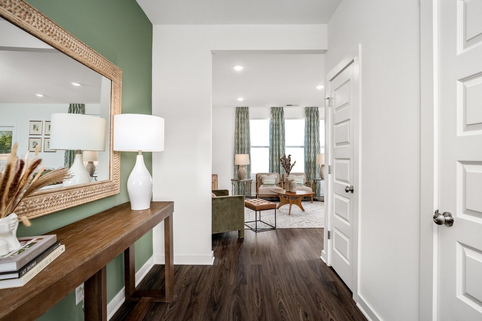 Entryway with wood console table and sage green wall leading to a bright living room in The Gordon C, Sage Farms home.