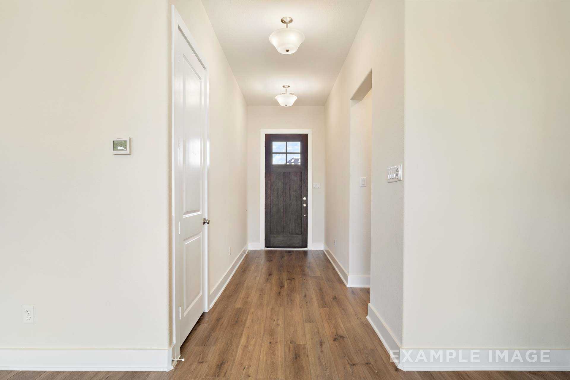Spacious entry hallway in The Diana C home with hardwood floors, neutral walls, dark wood door, and soft ceiling lights