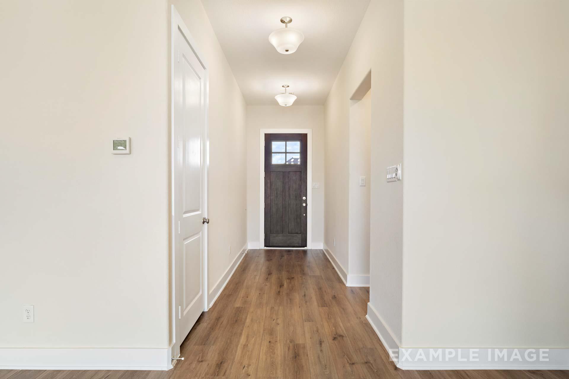 Spacious entry hallway in The Diana C home with hardwood floors, neutral walls, dark wood door, and soft ceiling lights