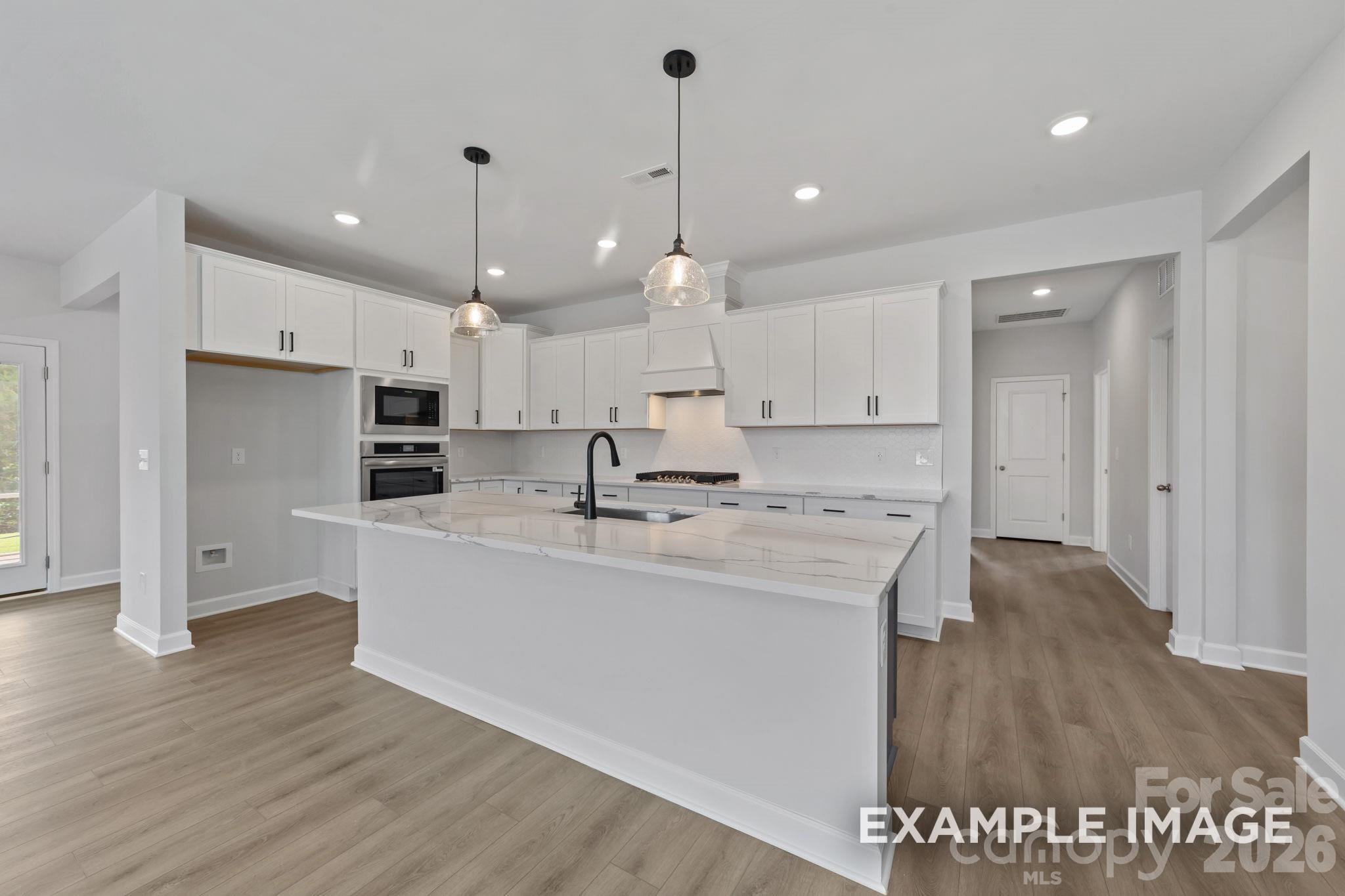 Modern kitchen with white cabinets, marble island, and pendant lighting in Davidson Homes Magnolia B plan, Mooresville, NC.