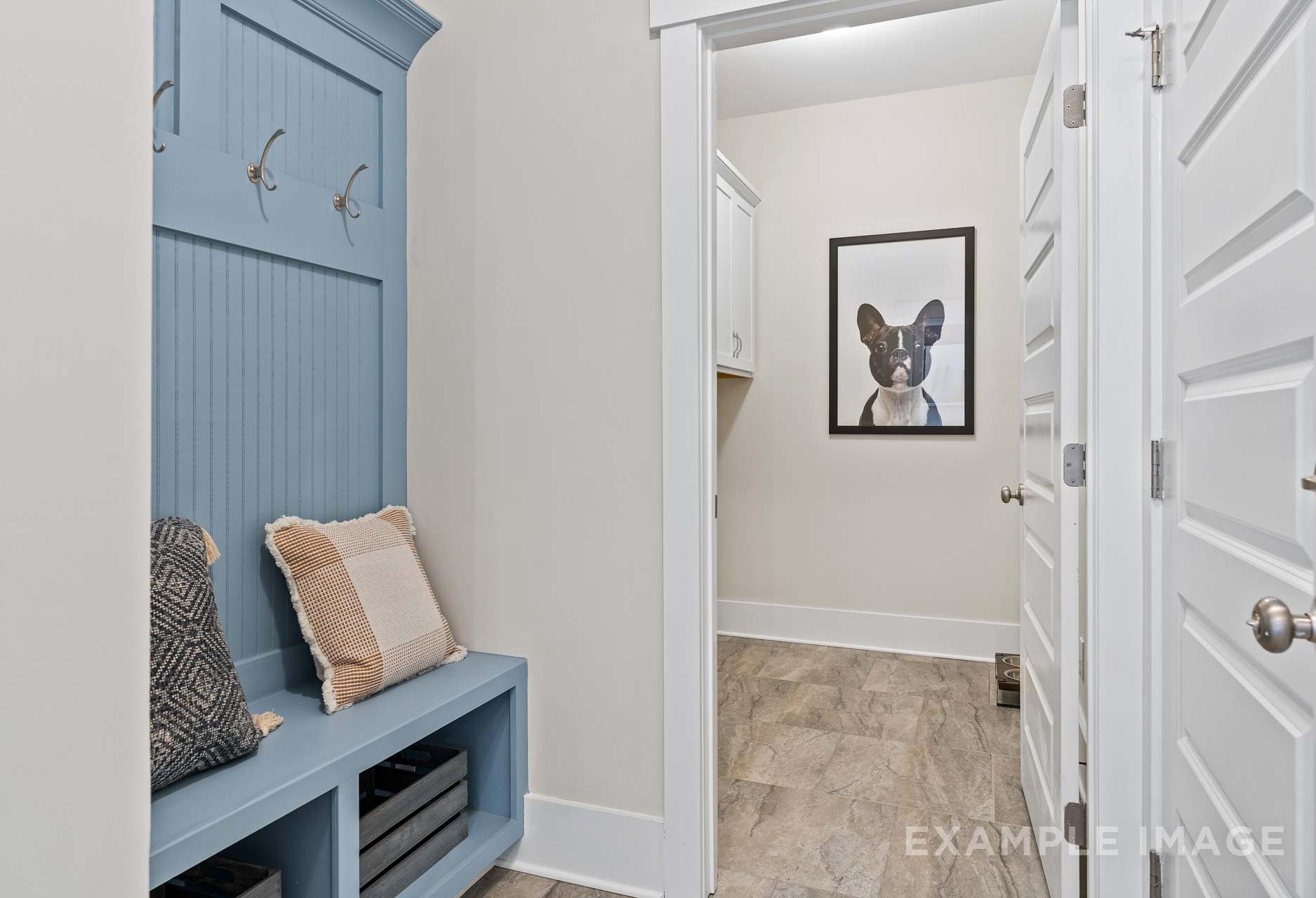 Spacious mudroom in The Rockford by Davidson Homes with blue shiplap locker, cushioned bench, and French Bulldog art