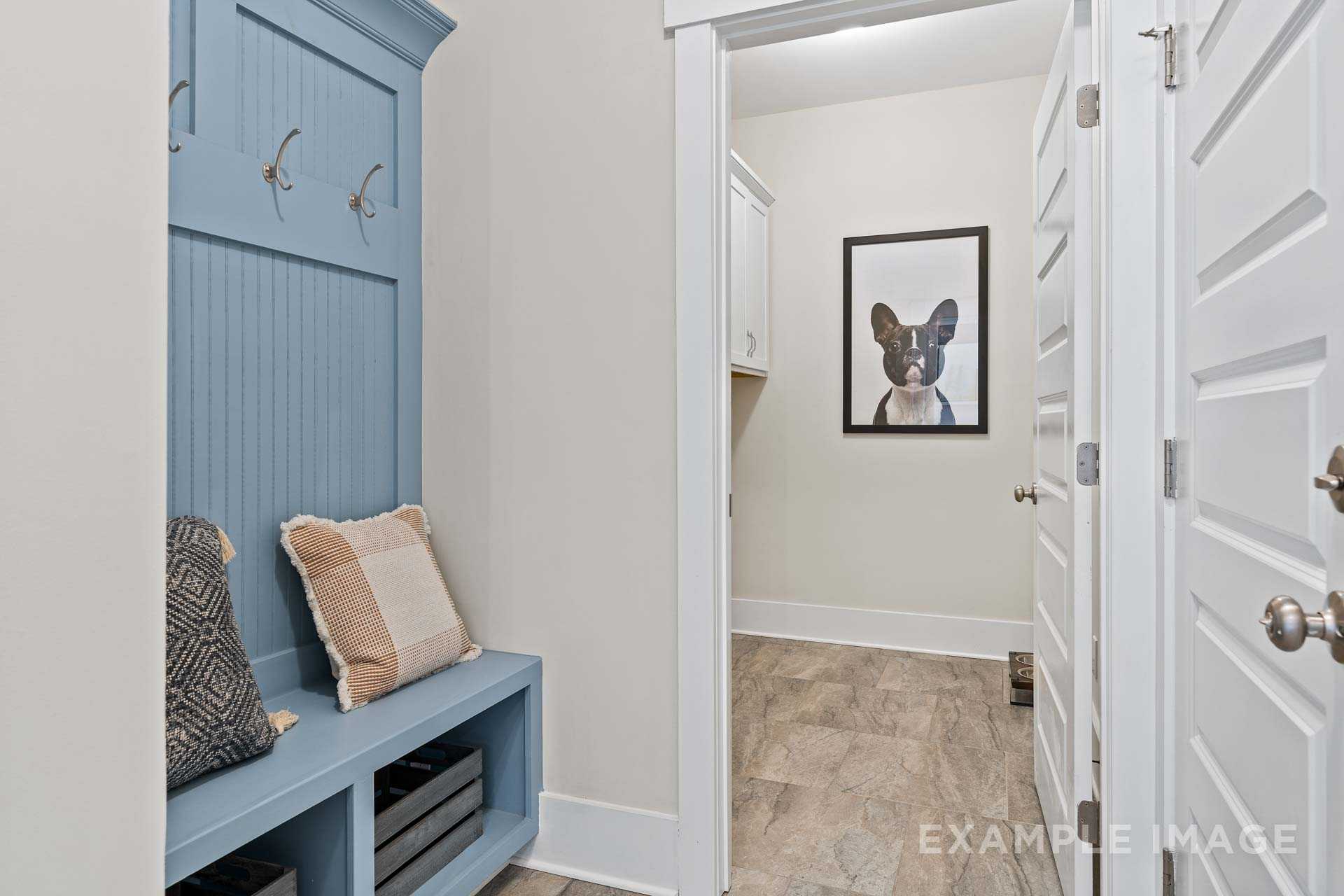 Spacious mudroom in The Rockford by Davidson Homes with blue shiplap locker, cushioned bench, and French Bulldog art