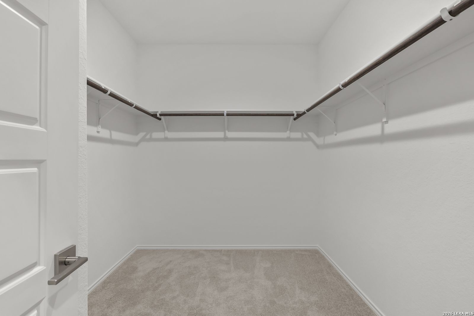 Spacious walk-in closet with wooden hanging rods and beige carpet in Davidson Homes The Glenwood E, Elmendorf, Texas