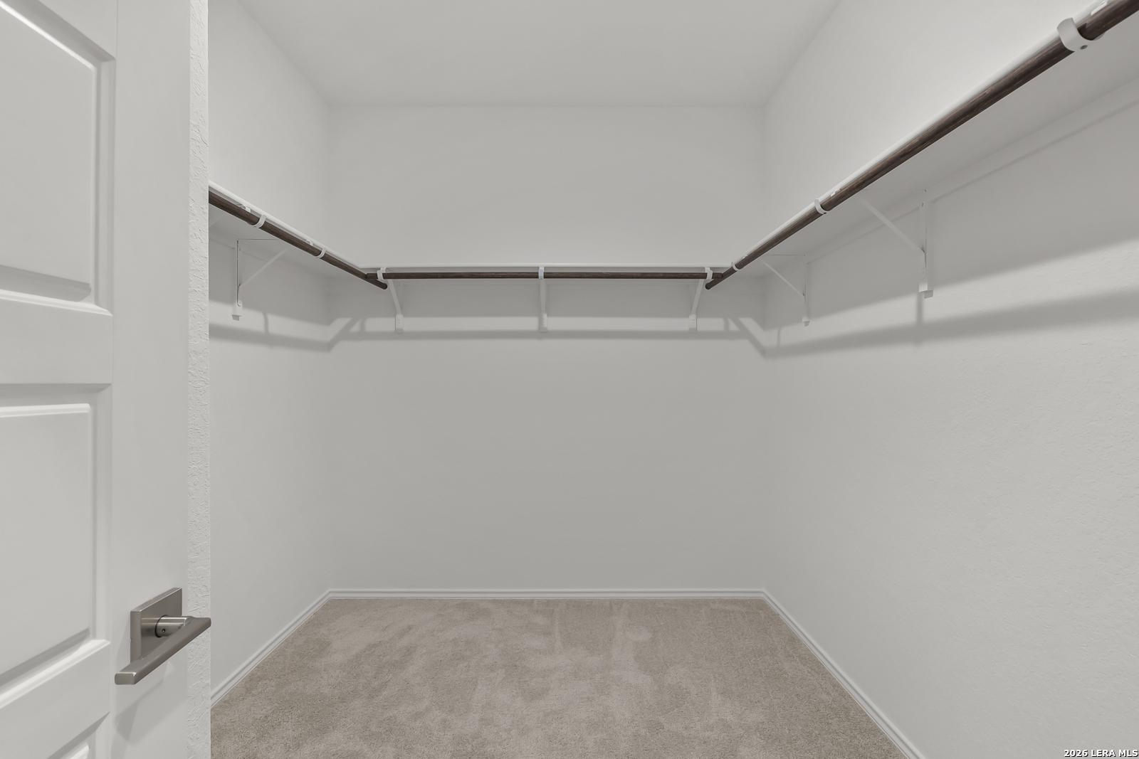 Spacious walk-in closet with wooden hanging rods and beige carpet in Davidson Homes The Glenwood E, Elmendorf, Texas