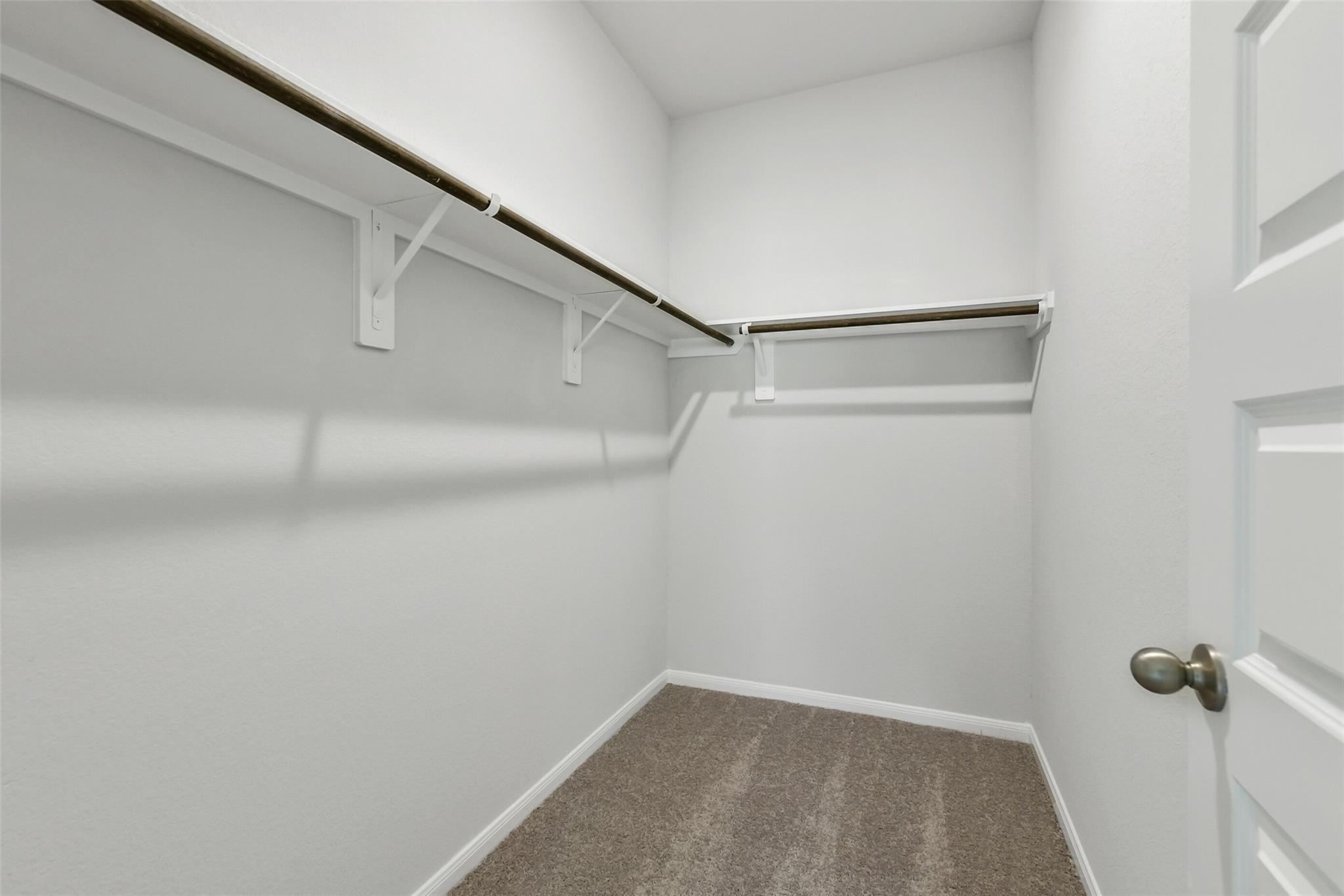 Spacious walk-in closet with wooden shelves, hanging rods, and beige carpet in Davidson Homes The Sabine E, Conroe, Texas
