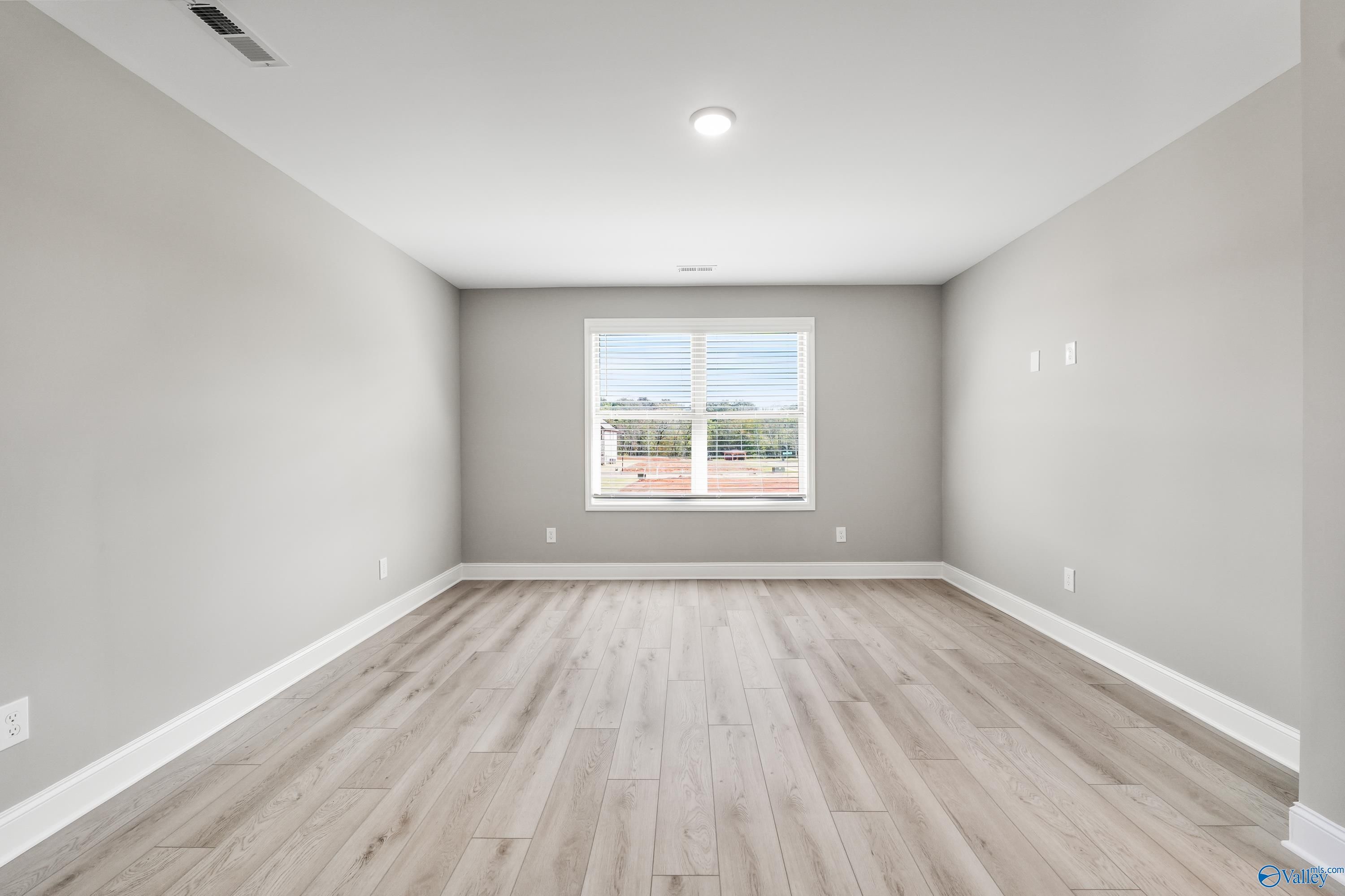 Bright secondary bedroom with light gray walls, oak hardwood floors, and large window overlooking greenery in The Everett B, Athens, Alabama