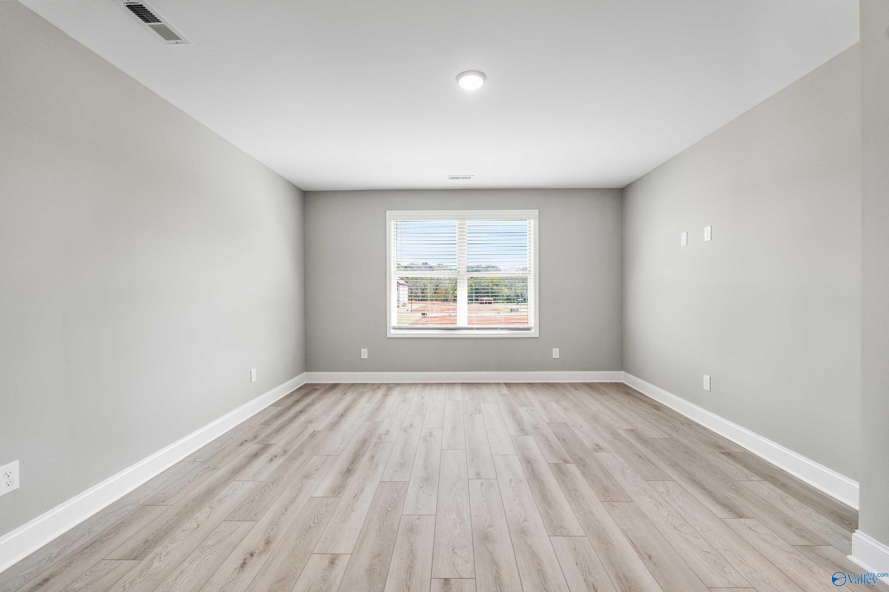 Empty bedroom with light gray walls, hardwood floors, and large window overlooking trees in Davidson Homes The Everett B, Athens, Alabama
