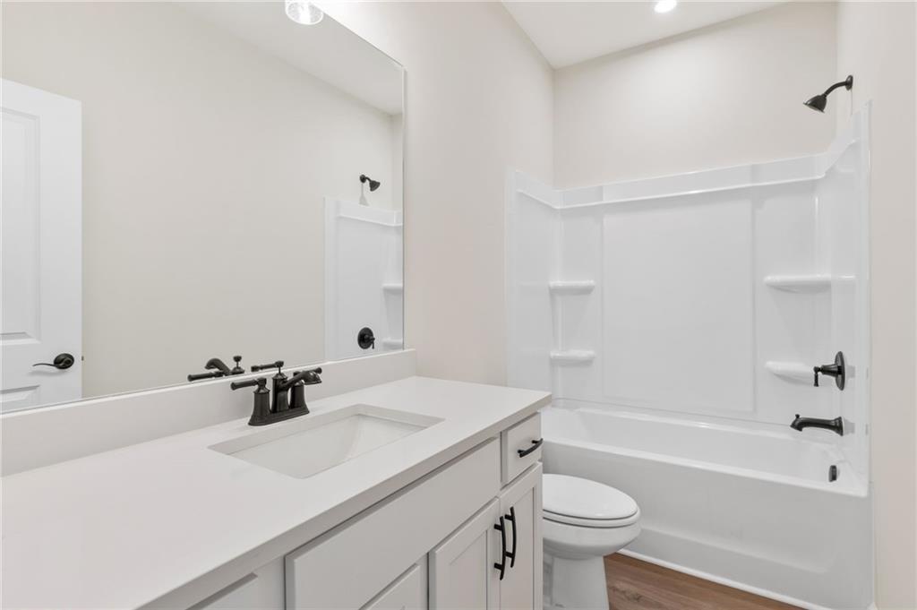 Bright modern bathroom with white vanity, soaking tub-shower combo, and hardwood floors in The Daphne B, Kelly Preserve, Loganville, GA