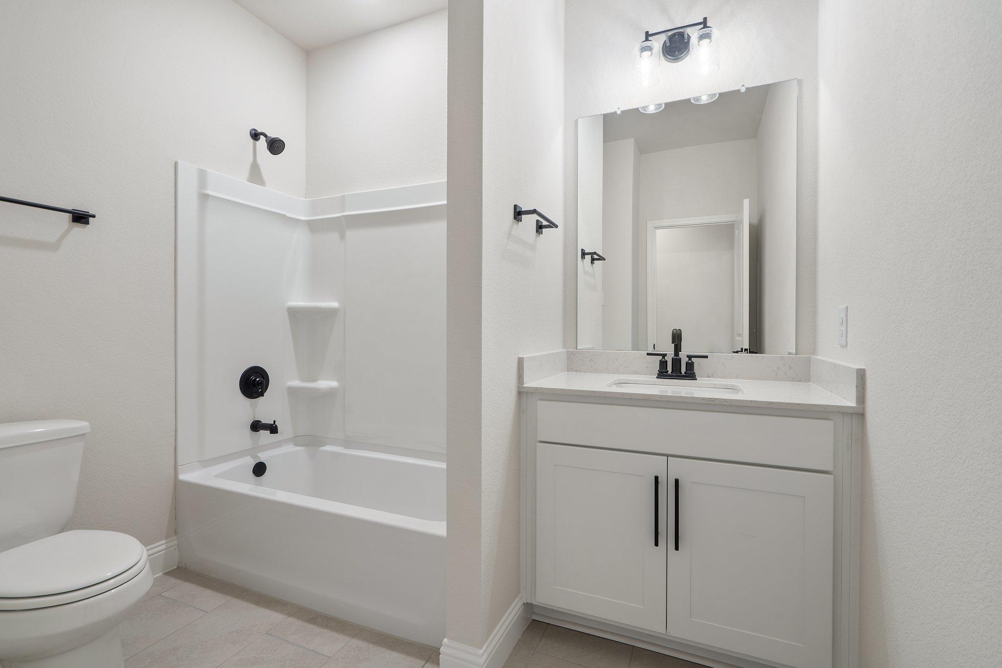 Modern bathroom in The Holly F home design featuring a white vanity, tub-shower combo, and sleek black fixtures.