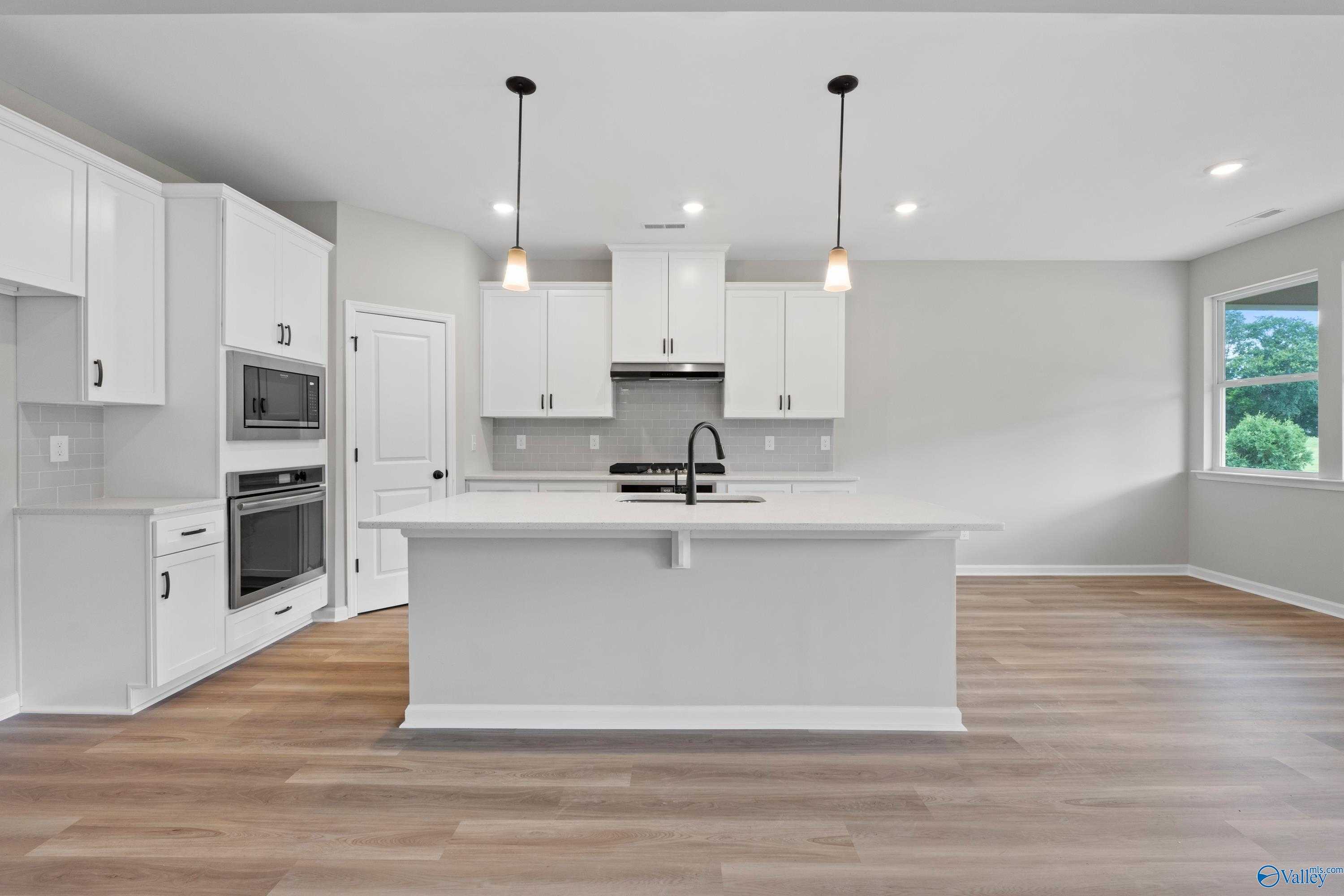 Modern white kitchen with large island sink, stainless appliances, hardwood floors in The Dorado plan, Riverton Preserve, Huntsville AL