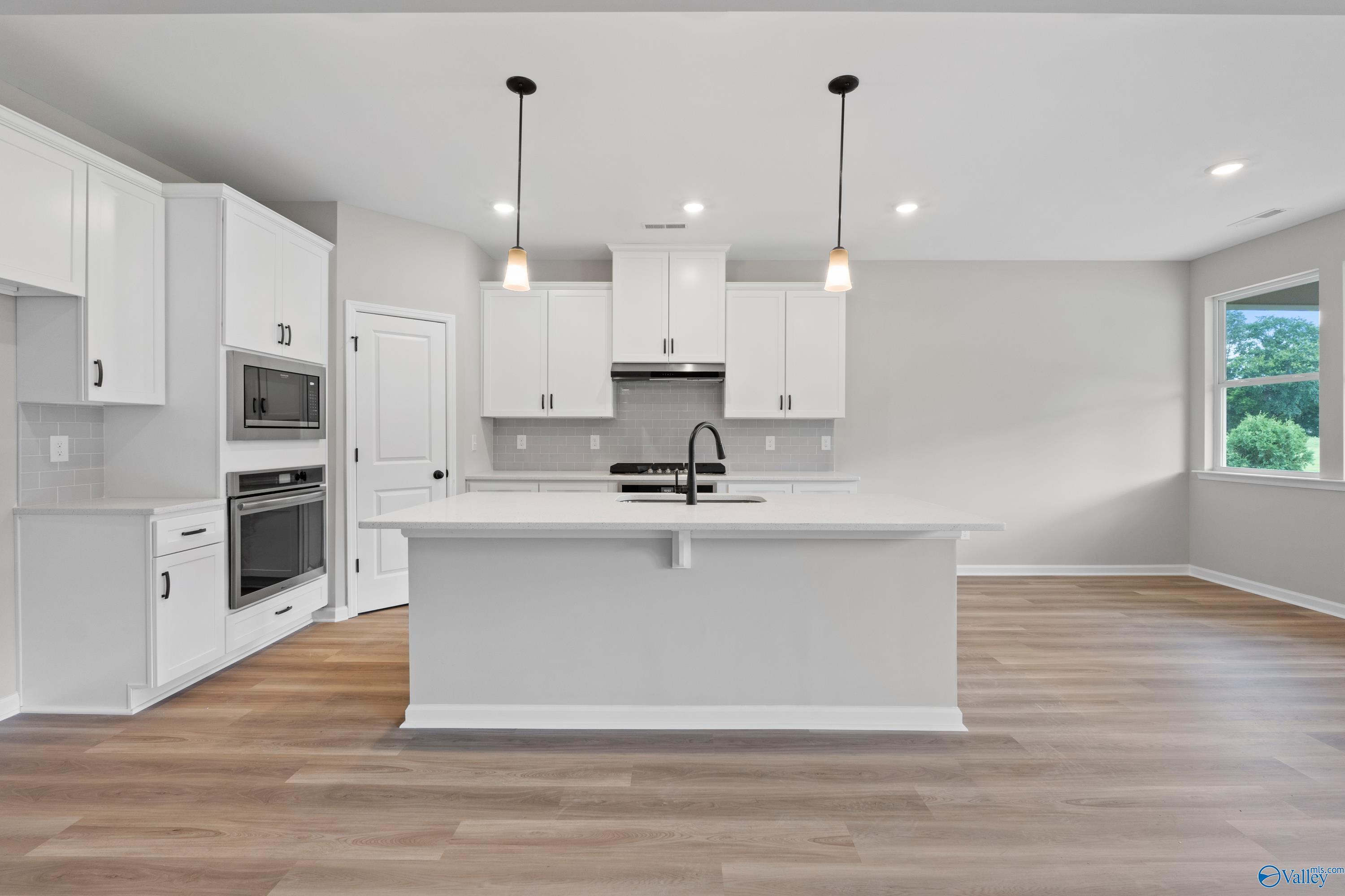 Modern white kitchen with large island sink, stainless appliances, hardwood floors in The Dorado plan, Riverton Preserve, Huntsville AL