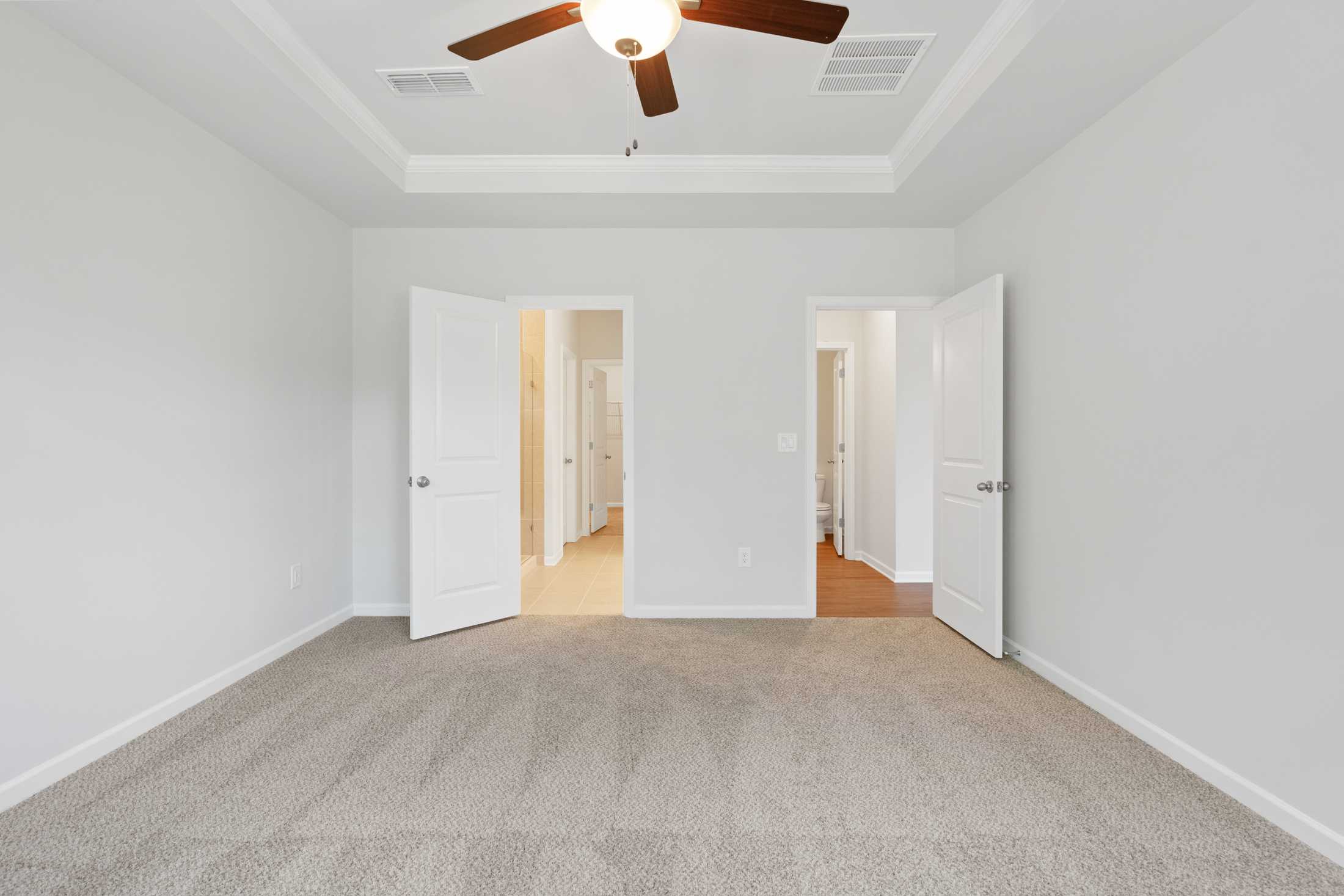 Spacious bedroom interior at Mountainbrook in Cartersville Georgia with tray ceiling fan, beige carpet, and open doors to ensuite bath and closet