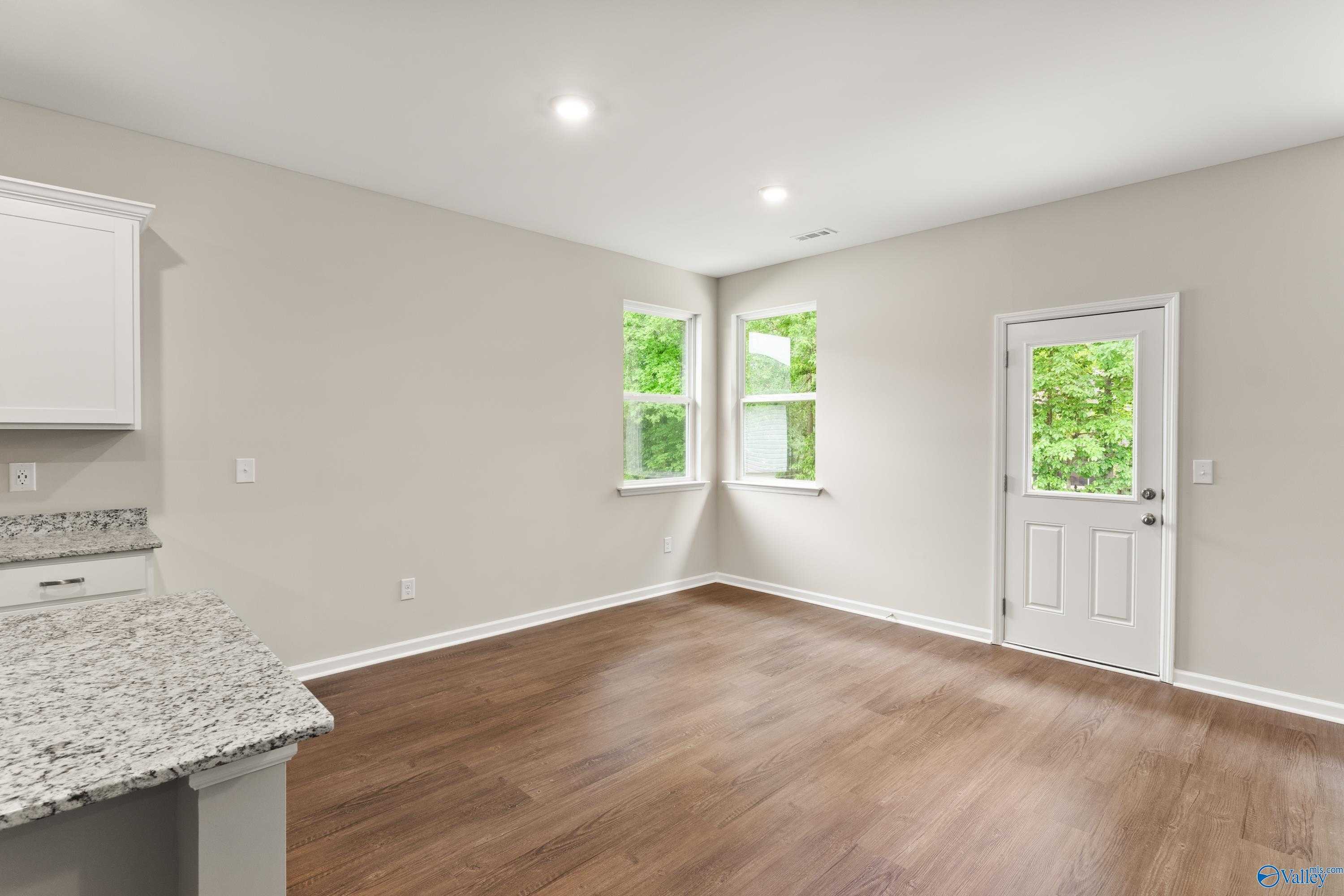 Bright kitchen corner with granite counters, white cabinets, hardwood floors, and glass door to yard in Davidson Homes The Phoenix, Fayetteville, TN