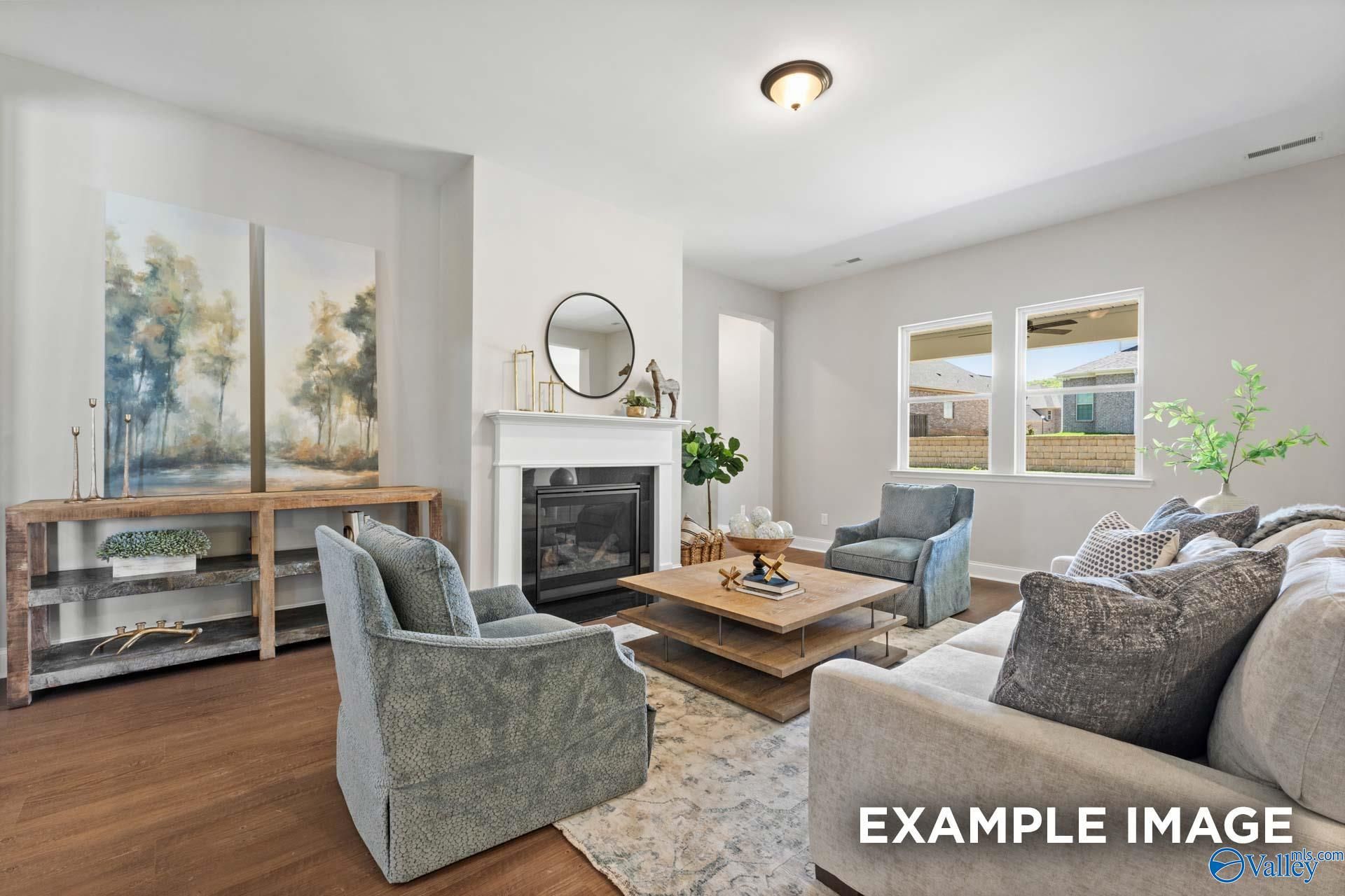 Cozy living room featuring white fireplace, abstract tree paintings, teal armchairs, gray sofa in Evermore Homes The Haven E, Owens Cross Roads, Alabama