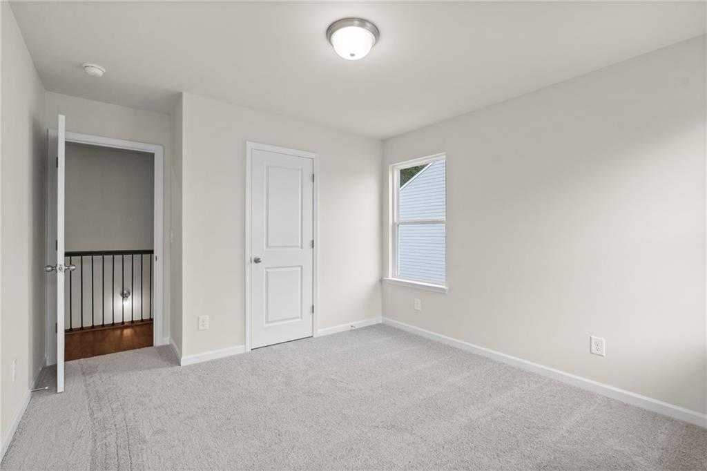 Bright upstairs bedroom with beige walls, carpet floor, window blinds, and stair railing in Davidson Homes The Marion B, Kennesaw, Georgia