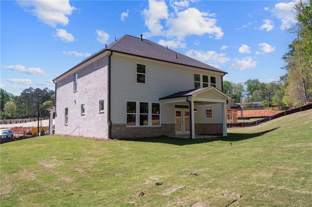 Two-story Hickory E home exterior with gray siding, brick base, covered patio, and lush green yard in Melody Lakeside Estates, Buford, Georgia