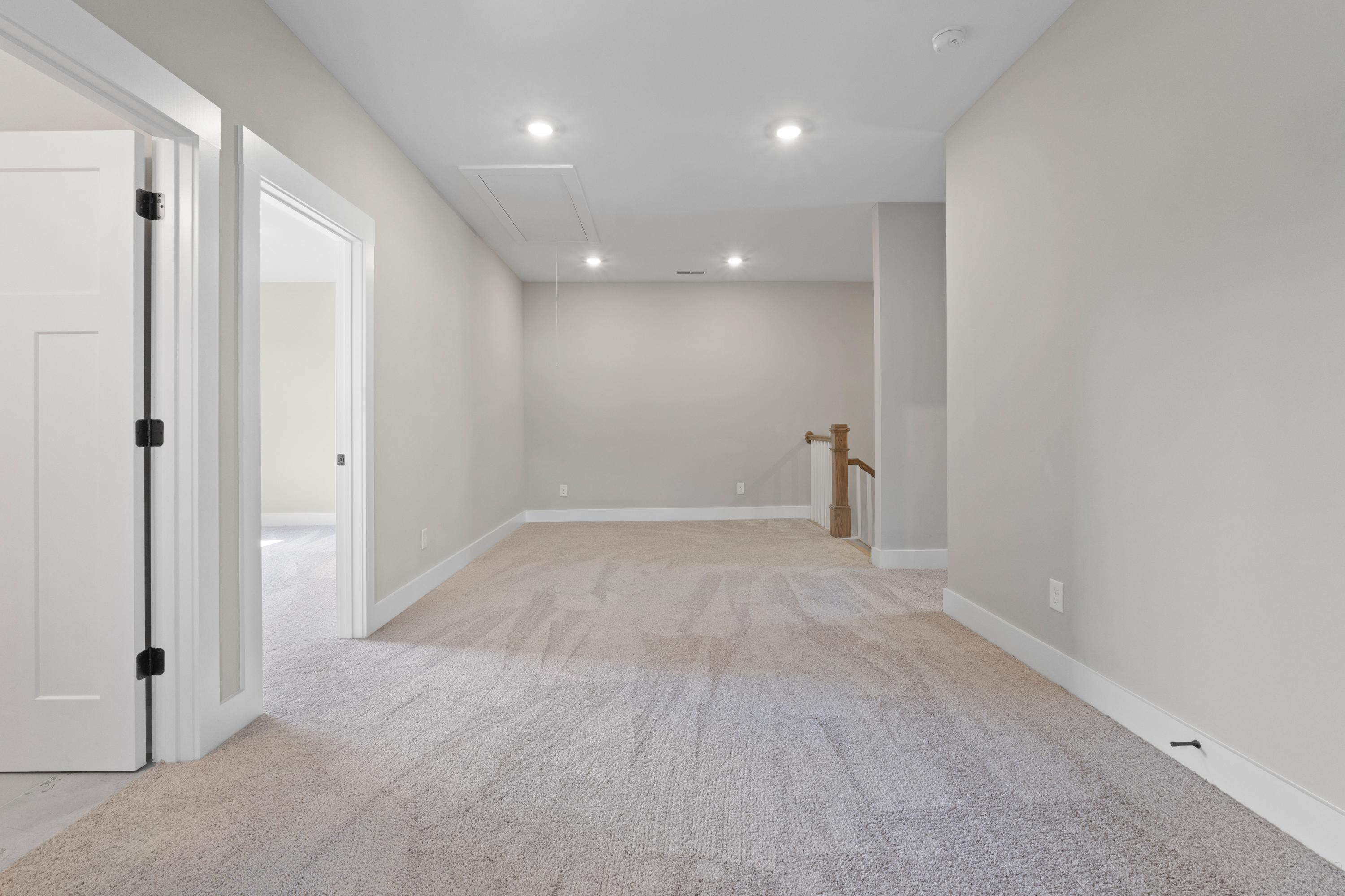 Spacious empty upstairs hallway in The Oxford home with beige carpet, light gray walls, white doors, recessed lights, wooden staircase