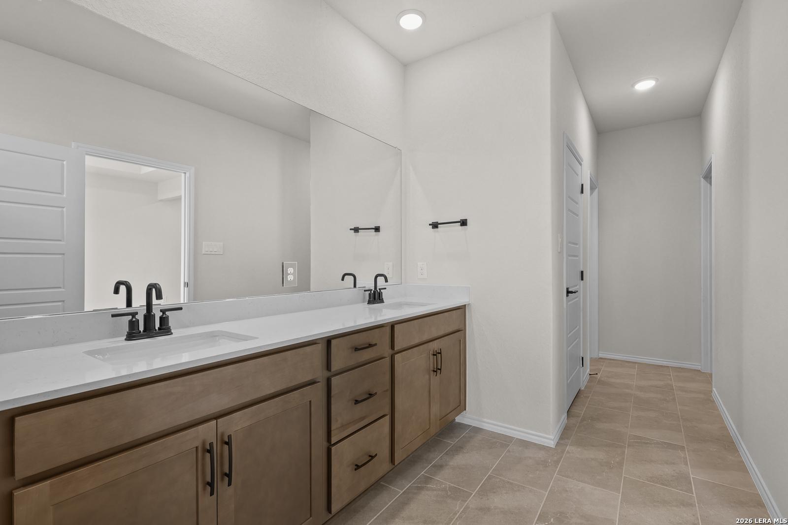 Double vanity bathroom with wood cabinets, quartz countertops, and tile flooring in Davidson Homes Glenwood E, San Antonio