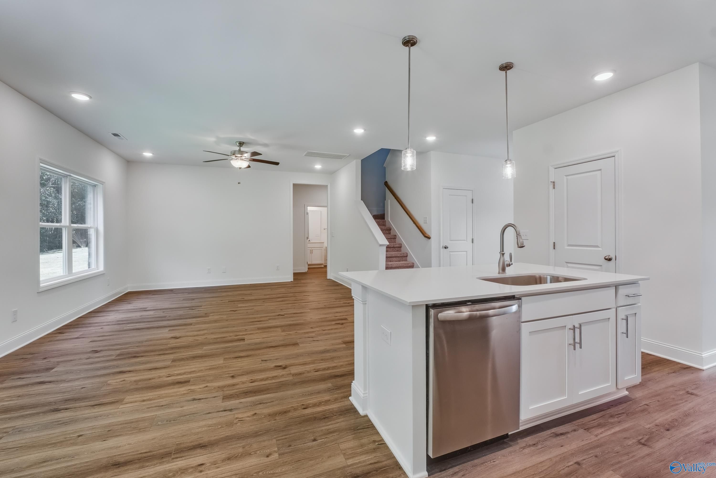 Open-concept kitchen with white island, stainless dishwasher, sink, hardwood floors, and stairs in Davidson Homes The Shelby A, Arab, Alabama