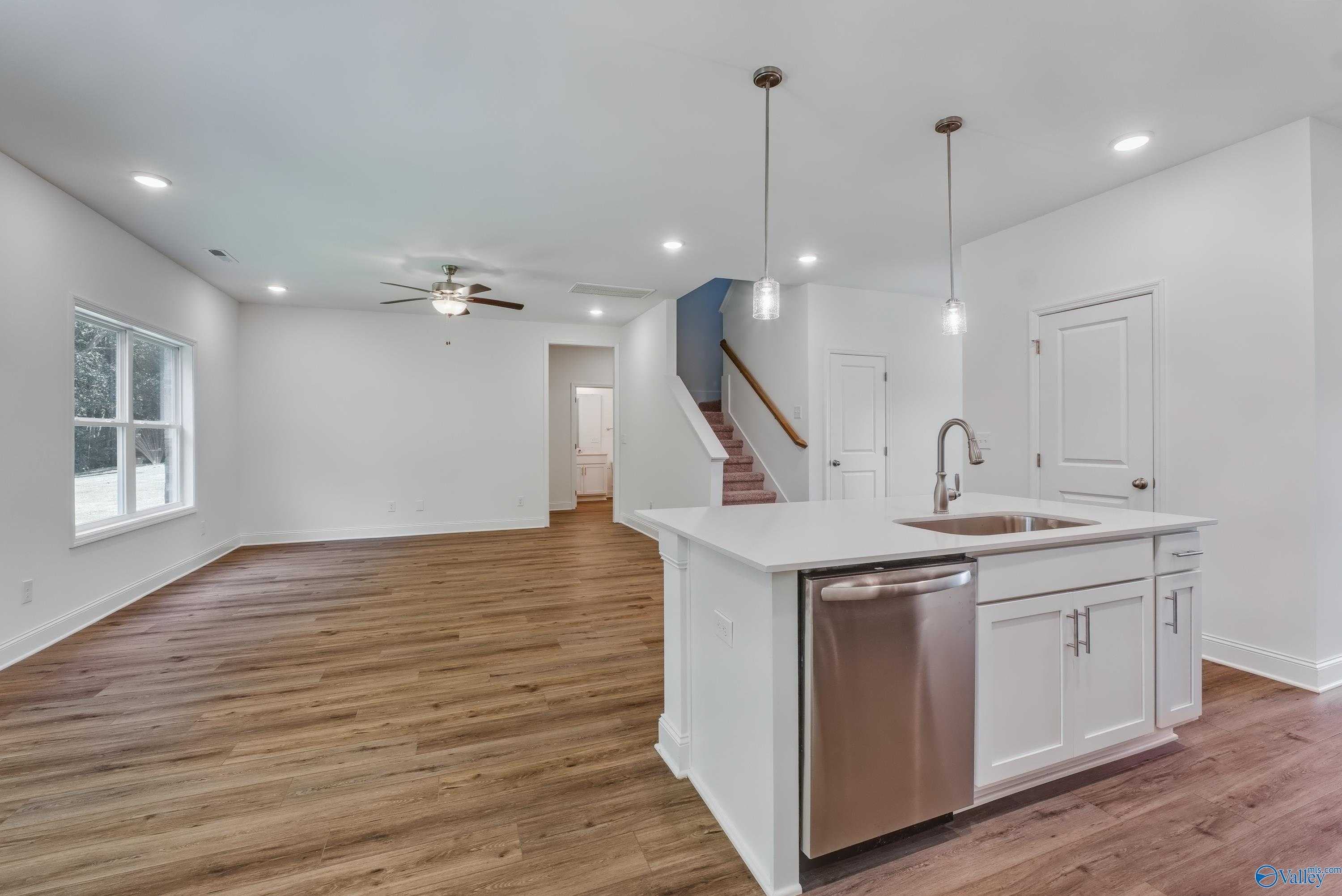Open-concept kitchen with white island, stainless dishwasher, sink, hardwood floors, and stairs in Davidson Homes The Shelby A, Arab, Alabama