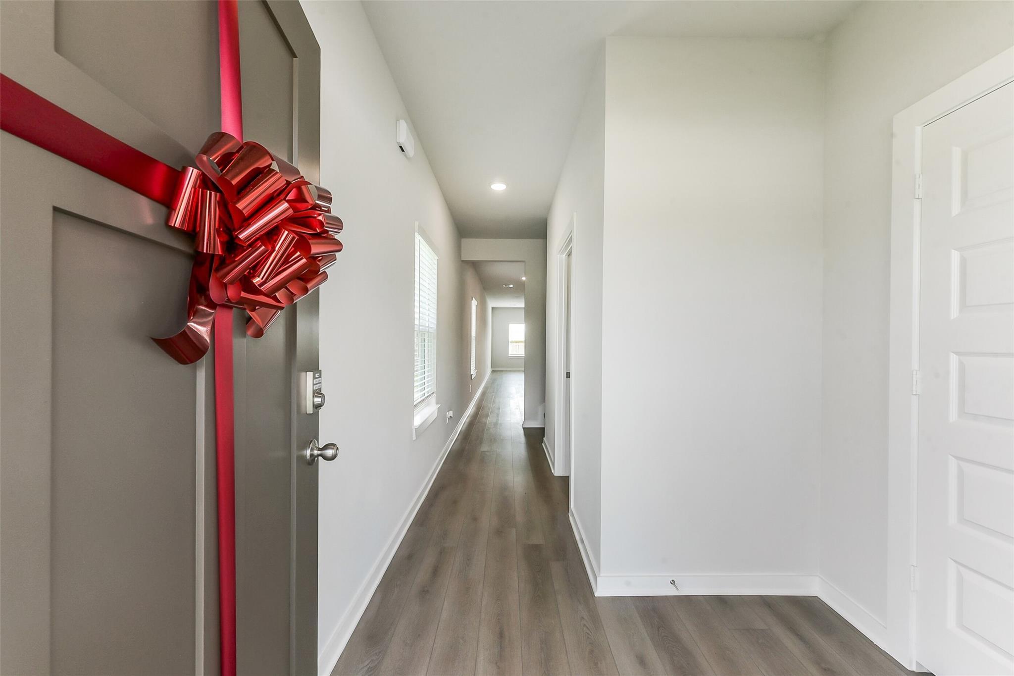 Spacious entry hallway with red ribbon bow on gray front door, white walls, recessed lights, gray laminate floors in Davidson Homes Sabine F, Dayton TX