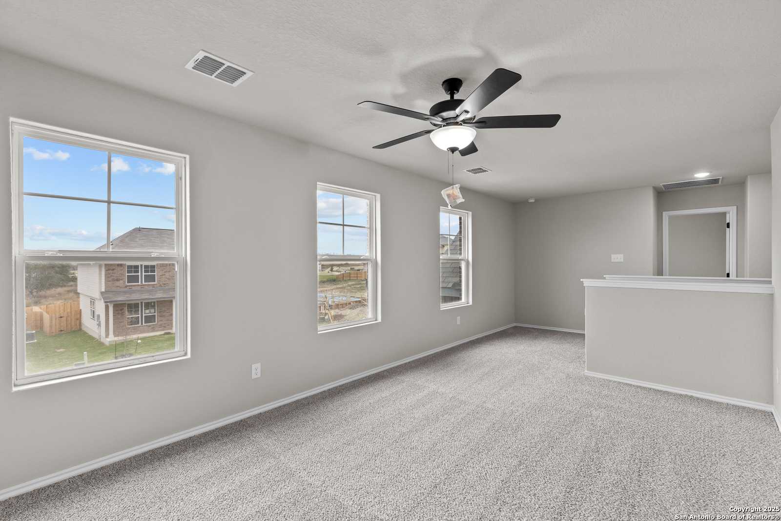 Spacious upstairs bonus room with gray carpet, large windows, ceiling fan, and bar counter in Davidson Homes The Murray I, San Antonio