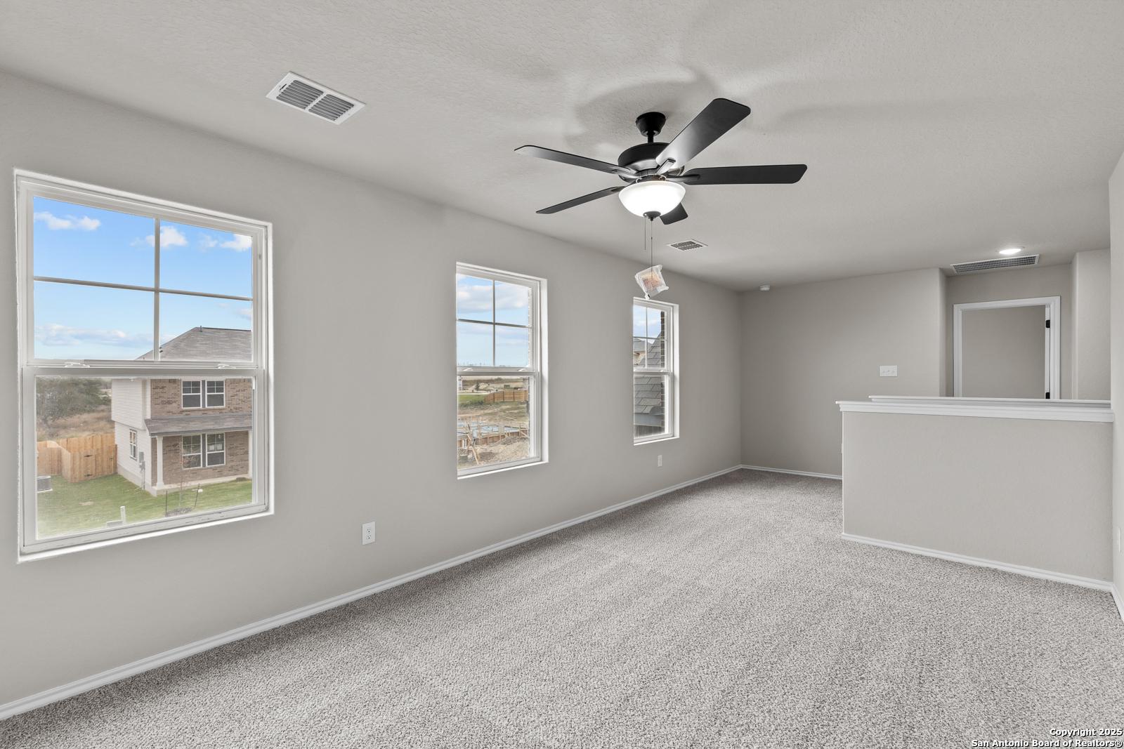 Spacious upstairs bonus room with gray carpet, large windows, ceiling fan, and bar counter in Davidson Homes The Murray I, San Antonio