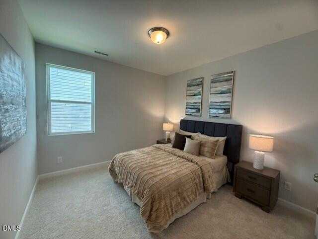 Spacious neutral bedroom with upholstered bed, bedside lamps, abstract art, and large window in The Preston C home, Lillington, NC