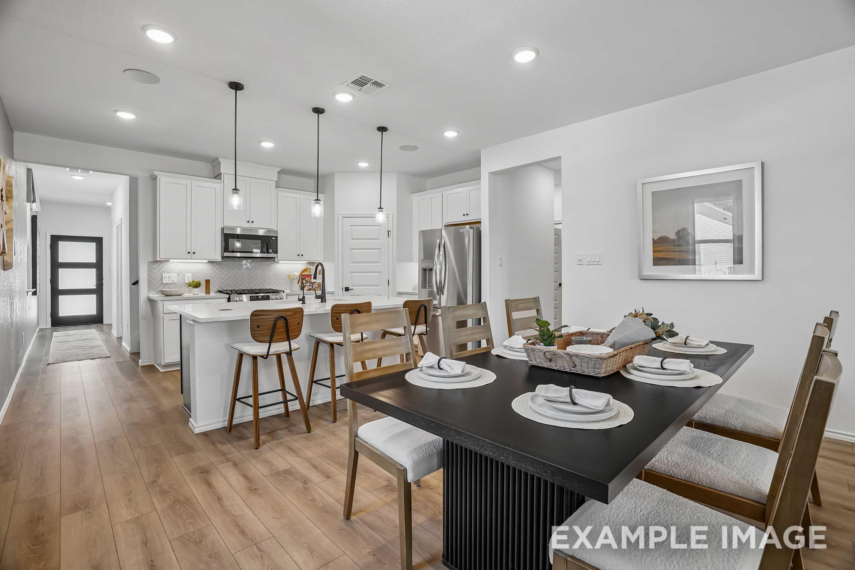 Open-concept kitchen and dining area in The Pinecrest featuring white cabinetry, large island, and modern dining furniture.