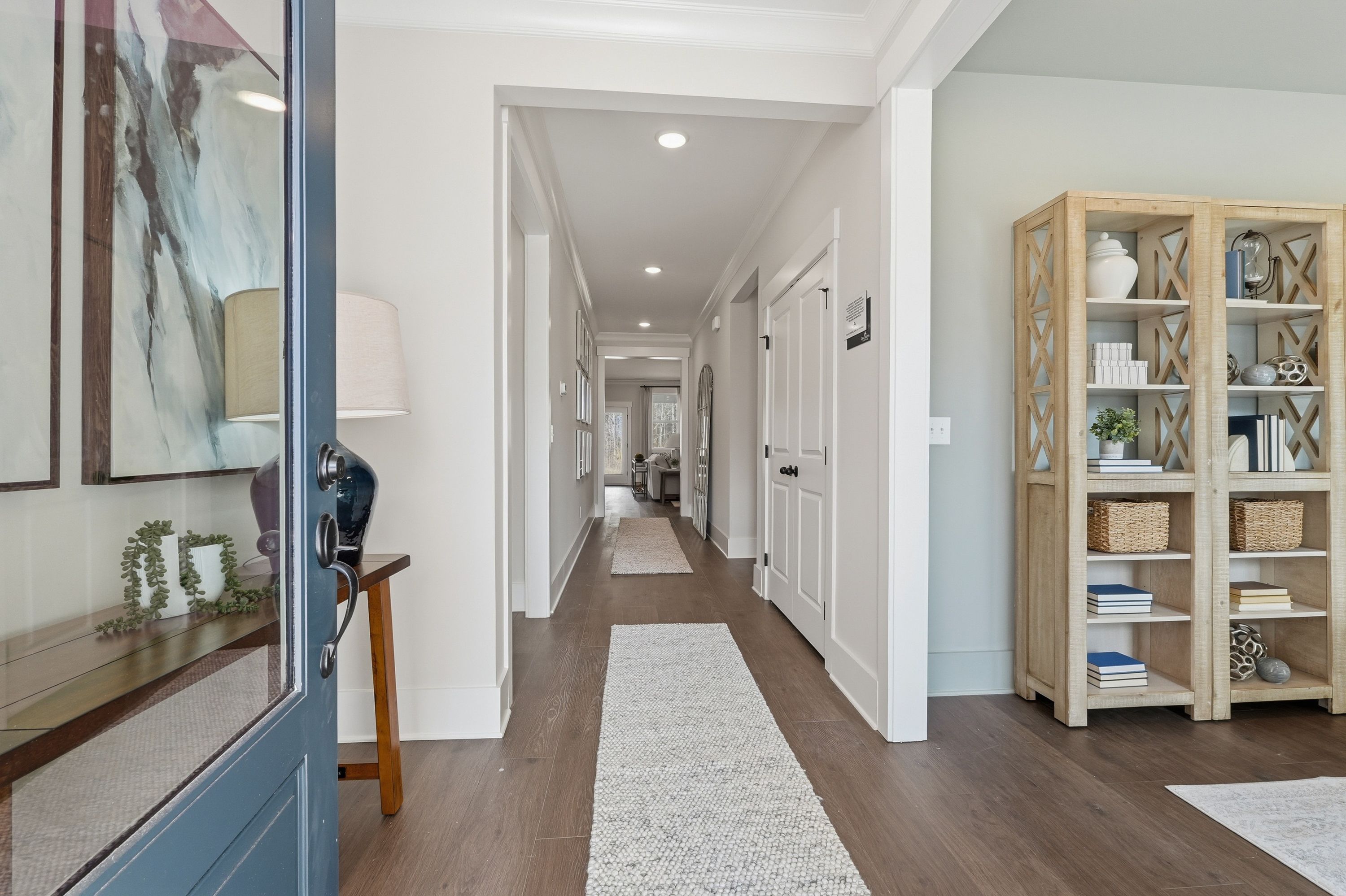Spacious entry hallway at Noble Ridge in Cullman AL with hardwood floors, blue front door, built-in shelving, and runner rug