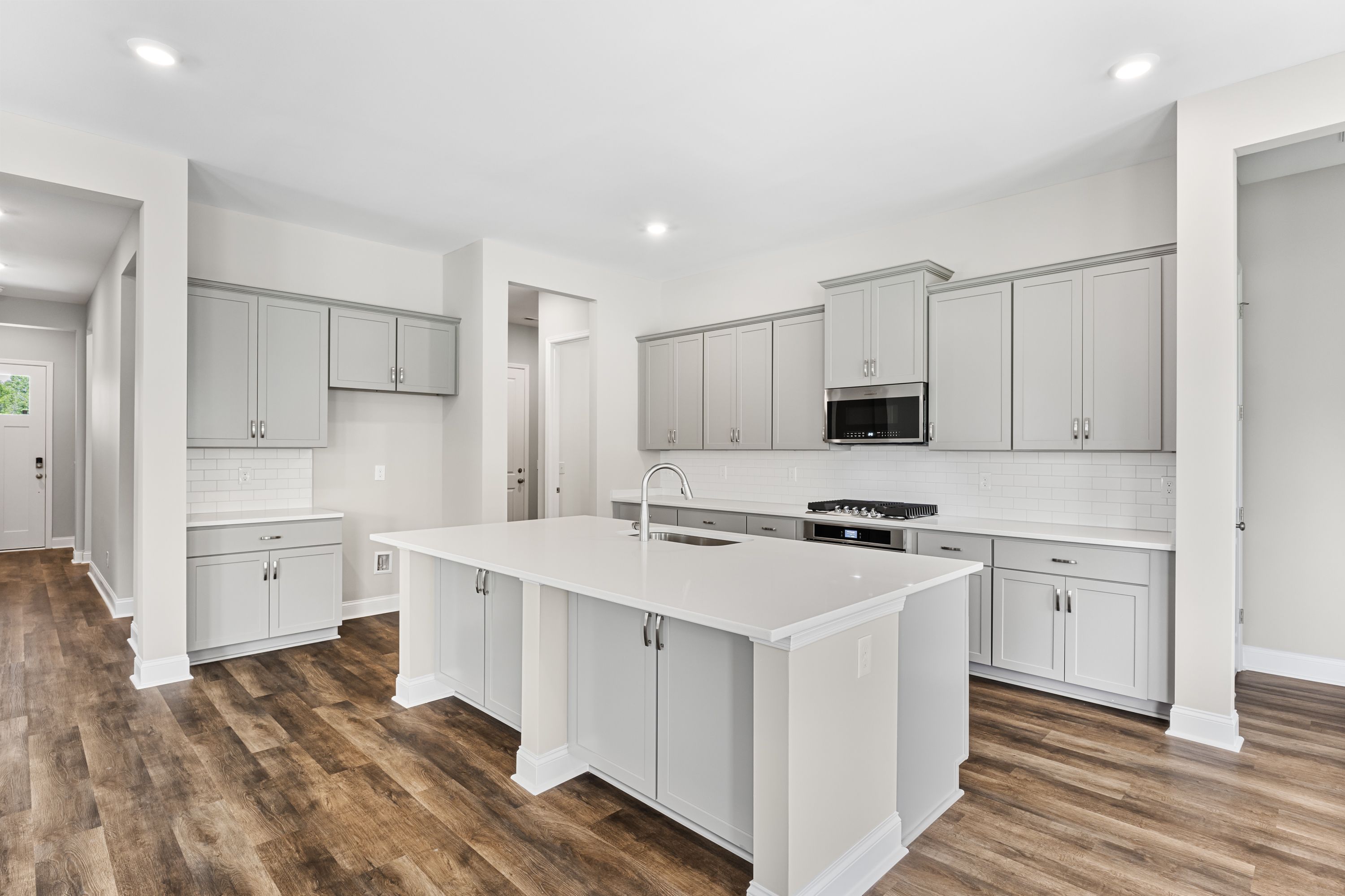 Spacious modern kitchen in The Arcadia E home with gray shaker cabinets, white quartz island, gas cooktop, and hardwood floors
