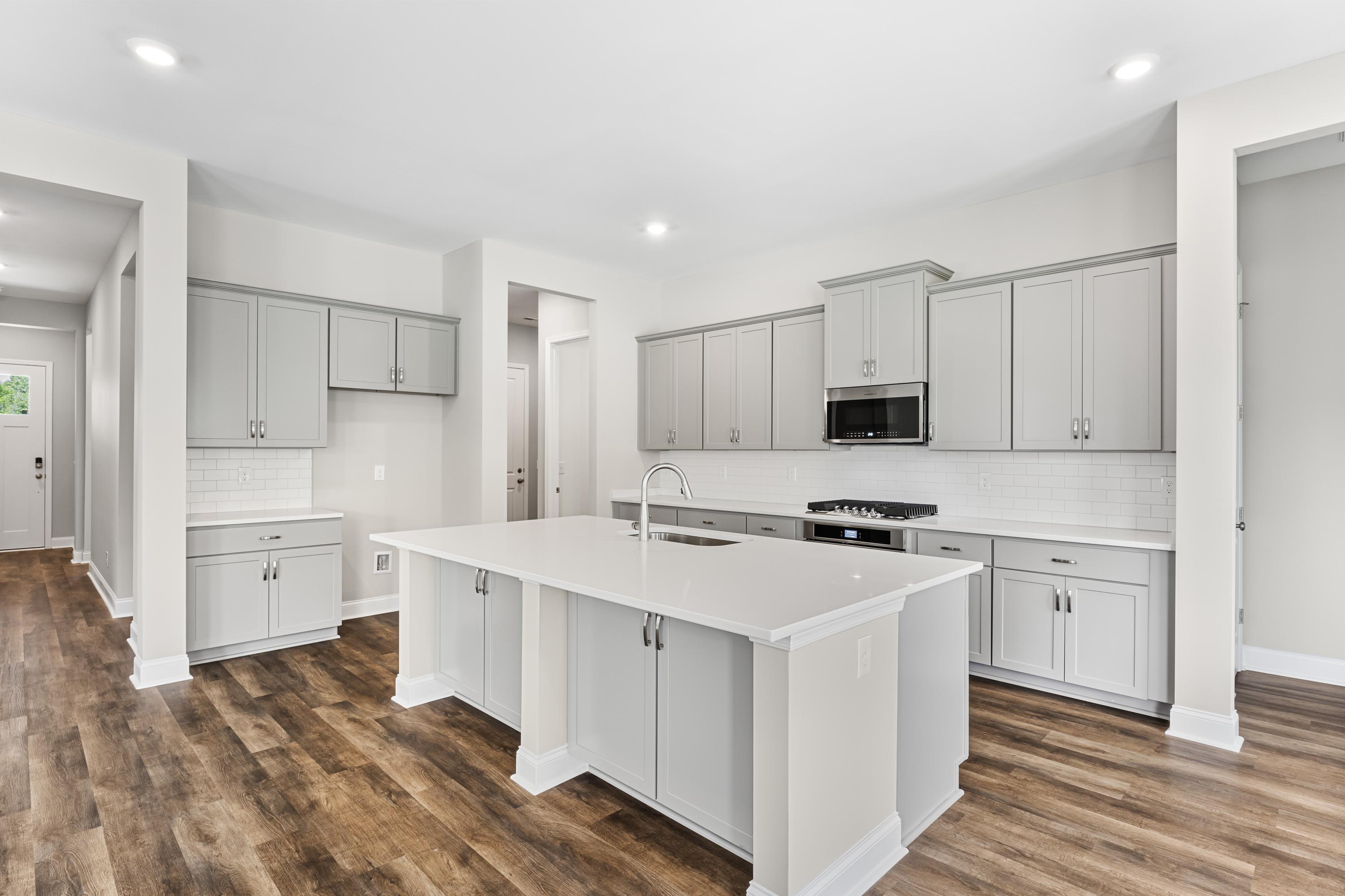 Spacious modern kitchen in The Arcadia B with large white island, shaker cabinets, gas range, and hardwood floors