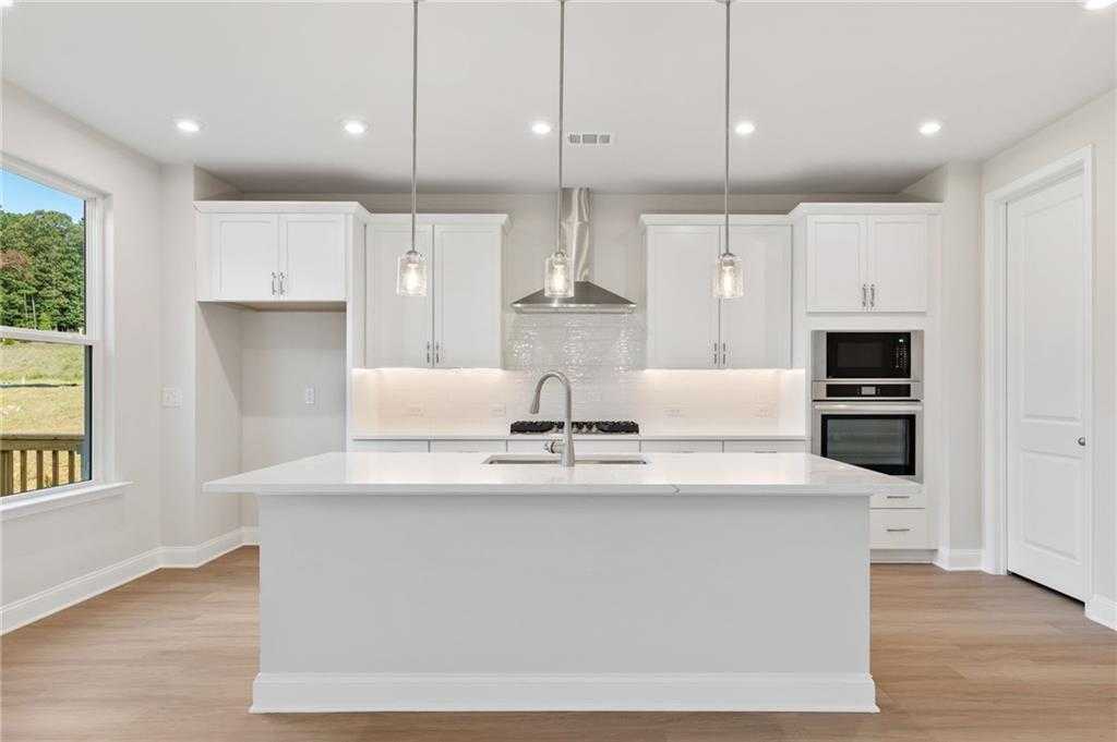 Modern white kitchen with large island, stainless appliances, pendant lights, and backyard view in The Hampton C, Buford, GA