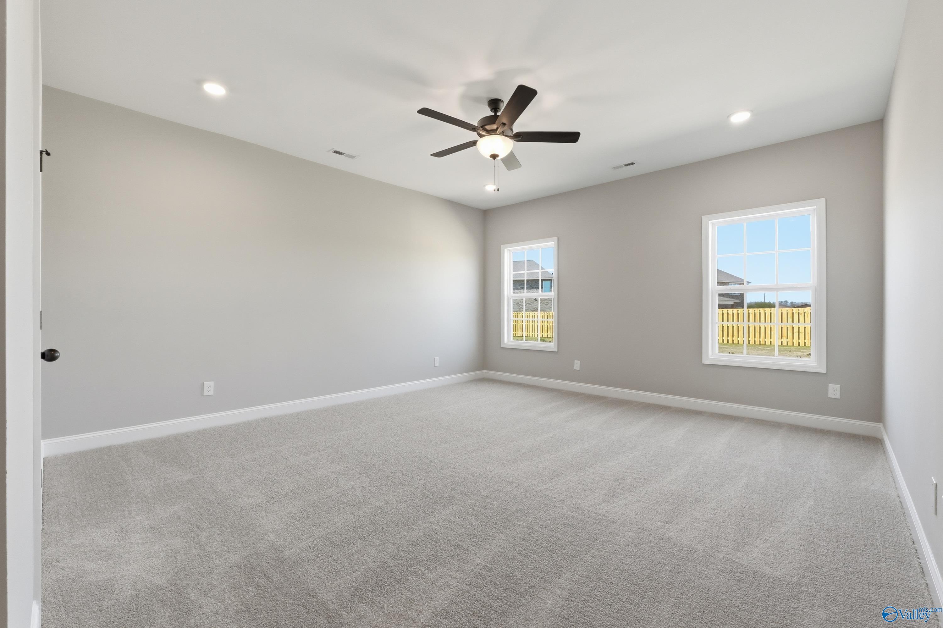 Spacious empty bedroom with gray walls, carpet flooring, ceiling fan, and large windows in Davidson Homes The Rockford, Harvest, Alabama