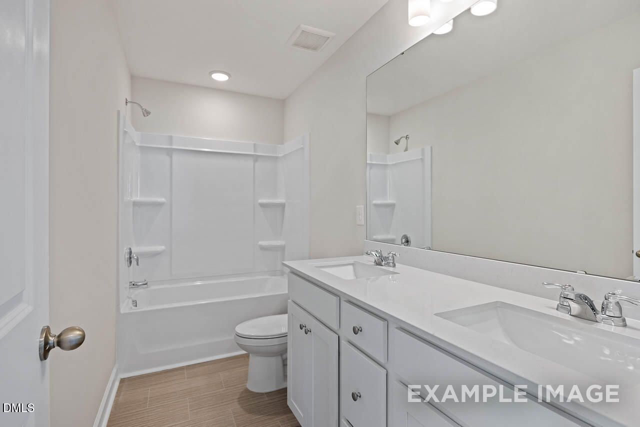 Modern bathroom with dual vanity, white cabinets, and tub-shower combo in The Graham floor plan at Springvale, Fuquay-Varina.