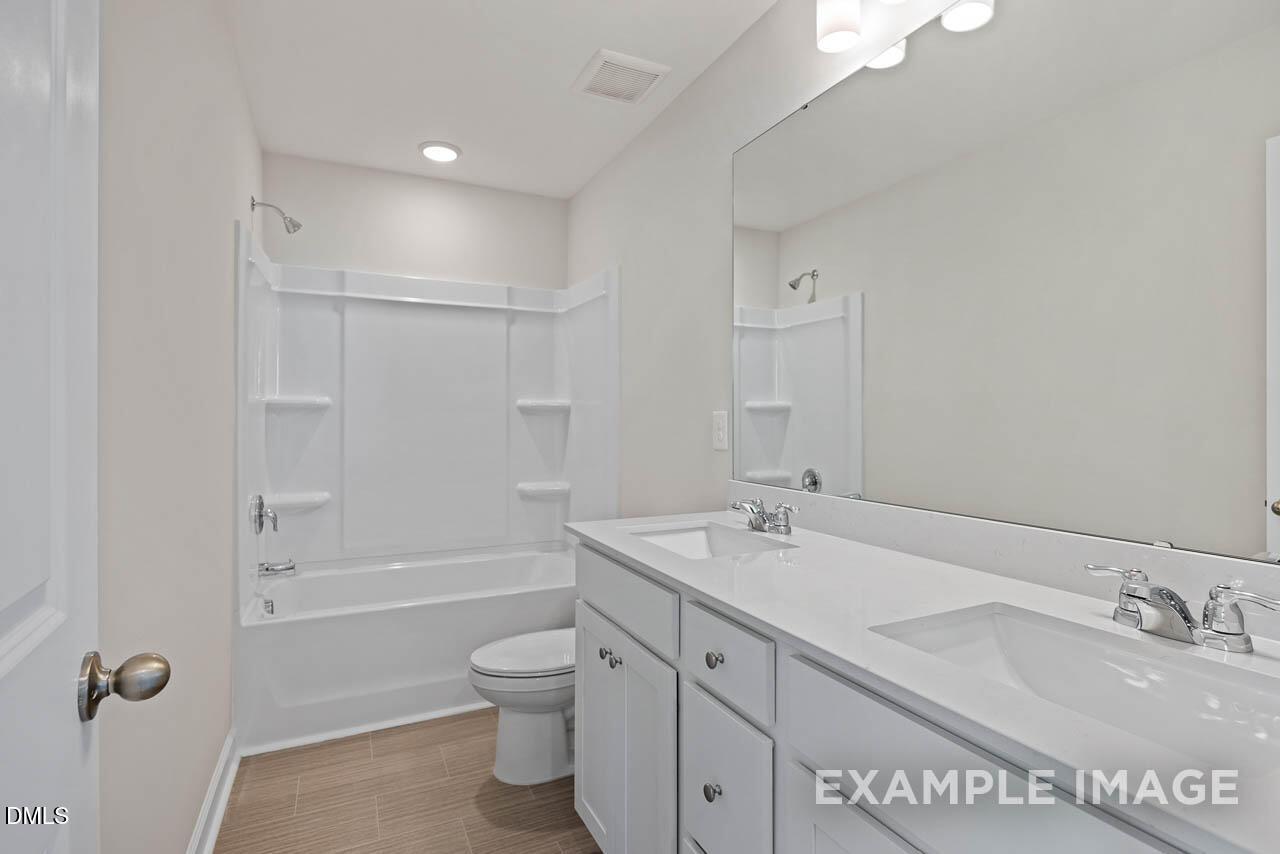 Modern bathroom with dual vanity, white cabinets, and tub-shower combo in The Graham floor plan at Springvale, Fuquay-Varina.