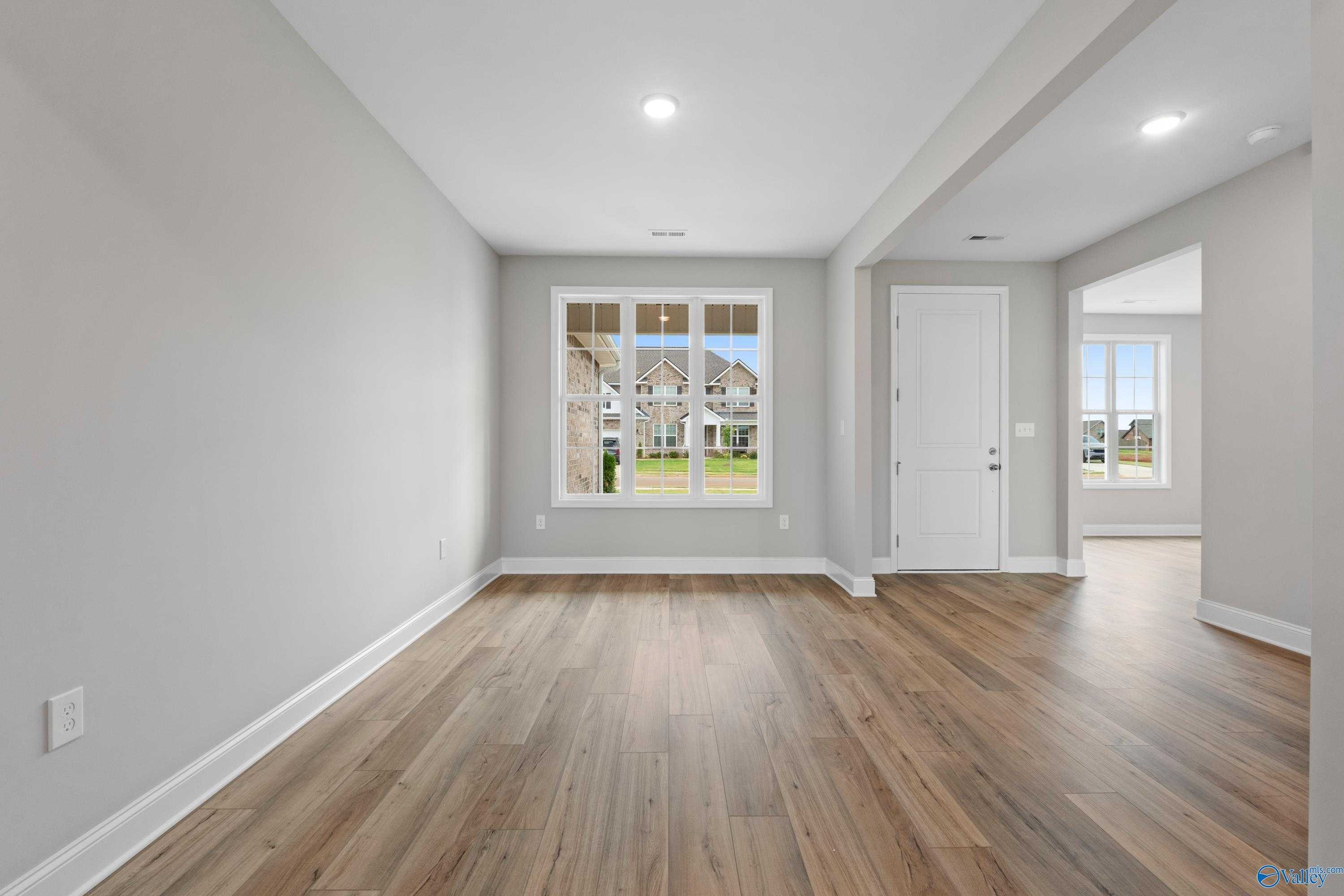 Spacious empty living room with gray walls, large window overlooking green yard, and light oak laminate floors in Davidson Homes The Finleigh, Meridianville, Alabama