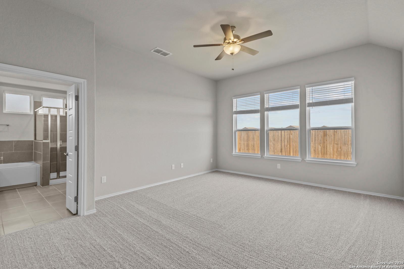 Spacious master bedroom with ceiling fan, large windows overlooking backyard, en-suite bath in The Collin B, Seguin, Texas