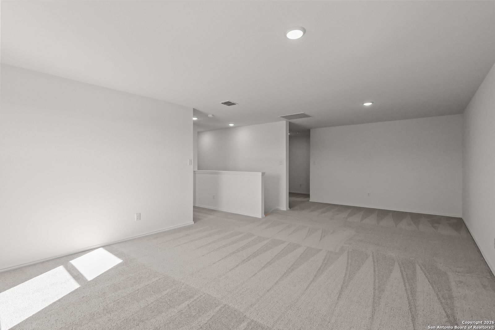 Spacious carpeted upstairs loft with white walls, recessed lights, and balcony railing in Davidson Homes The Douglas E, San Antonio