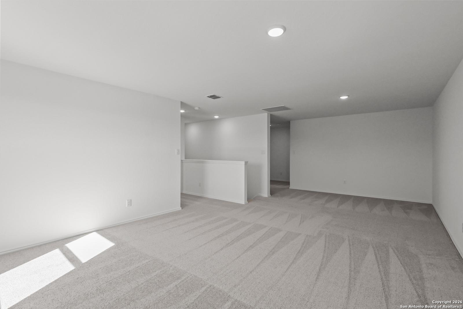 Spacious carpeted upstairs loft with white walls, recessed lights, and balcony railing in Davidson Homes The Douglas E, San Antonio