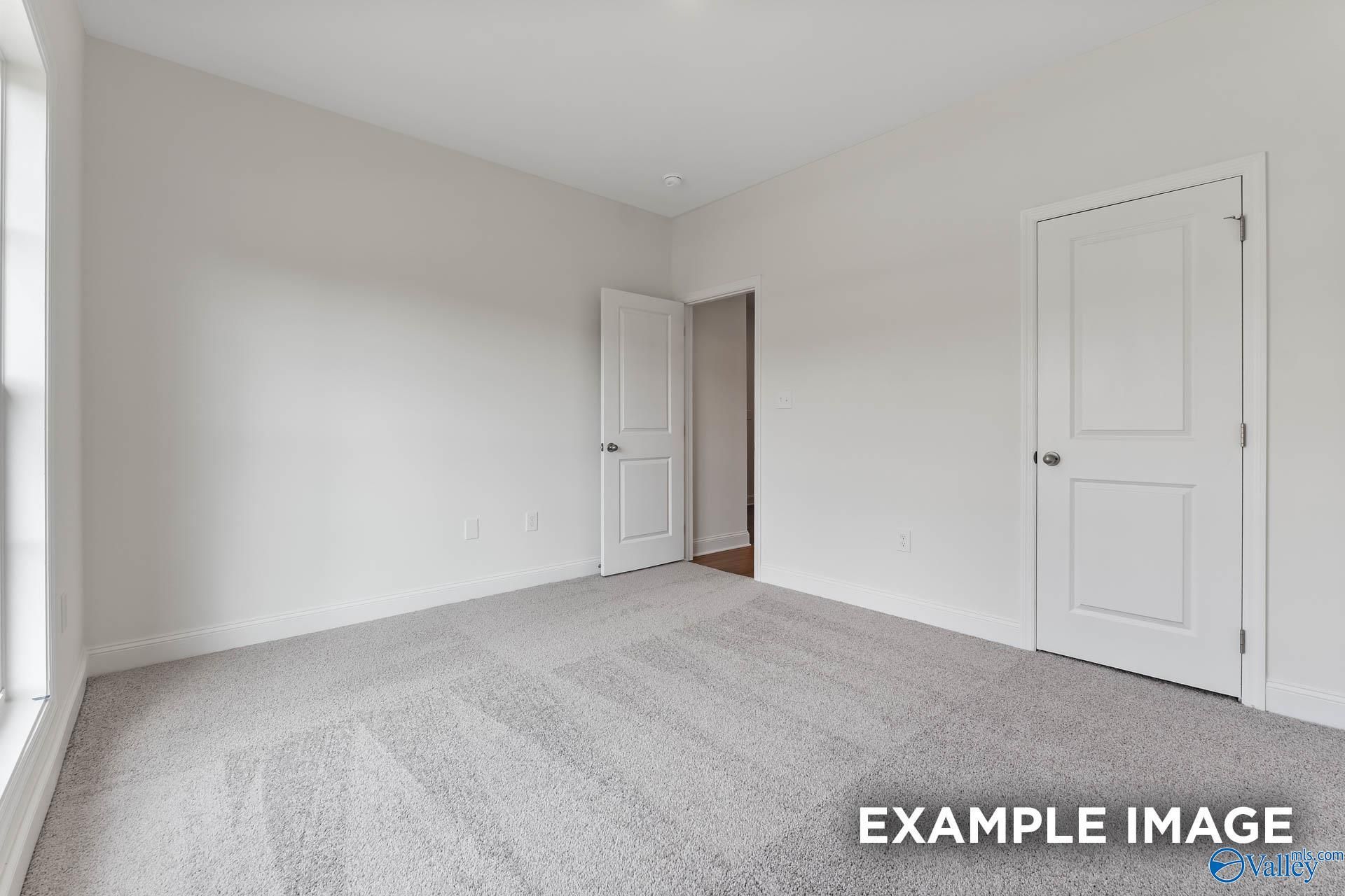 Empty bedroom with white walls, beige carpet, double doors, and large window in Davidson Homes The Daphne V, Athens, Alabama